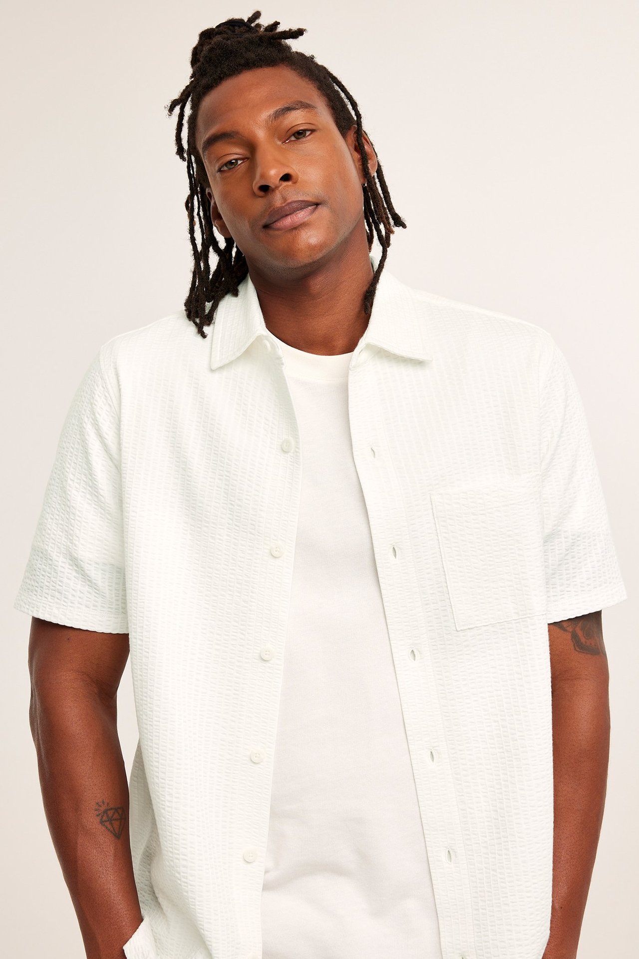 Widok z przodu: Mężczyzna w kremowej, teksturowanej koszuli z krótkim rękawem i kieszenią, na białym t-shircie.