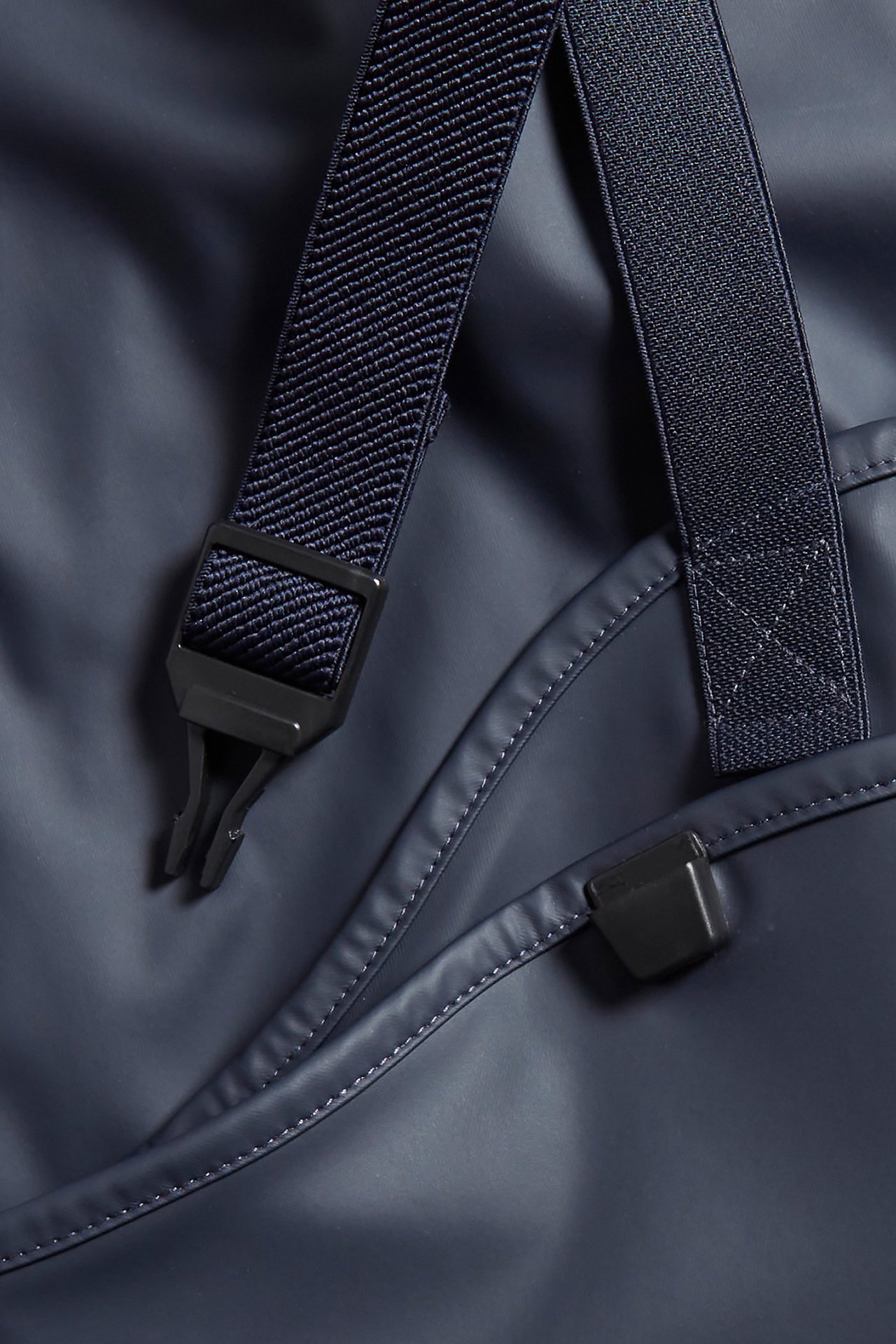 Zbliżenie na niebieskie dziecięce spodnie przeciwdeszczowe z granatowymi elastycznymi szelkami i czarnymi klamrami.