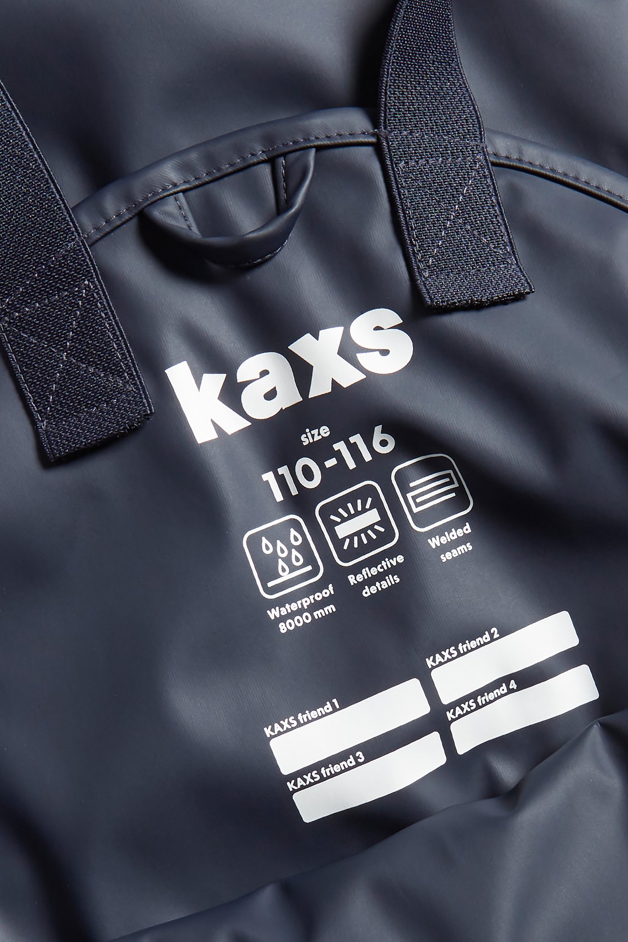 Närbild på mörkblå fleecefodrade regnbyxor med Kaxs-logga, hängslen och vattentäta detaljer.
