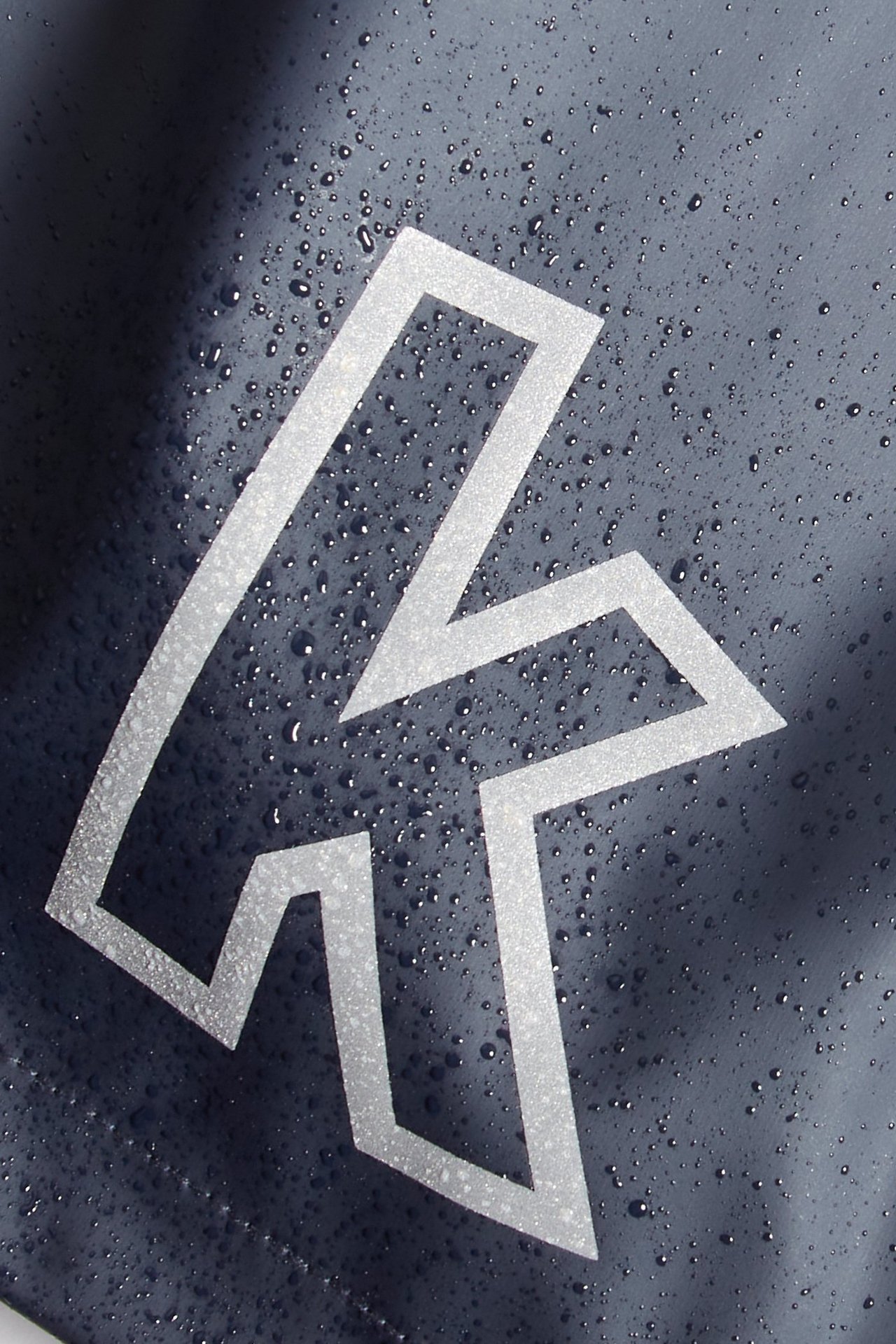 Zbliżenie na ciemnoniebieską kurtkę przeciwdeszczową z kroplami wody i białym odblaskowym logo.