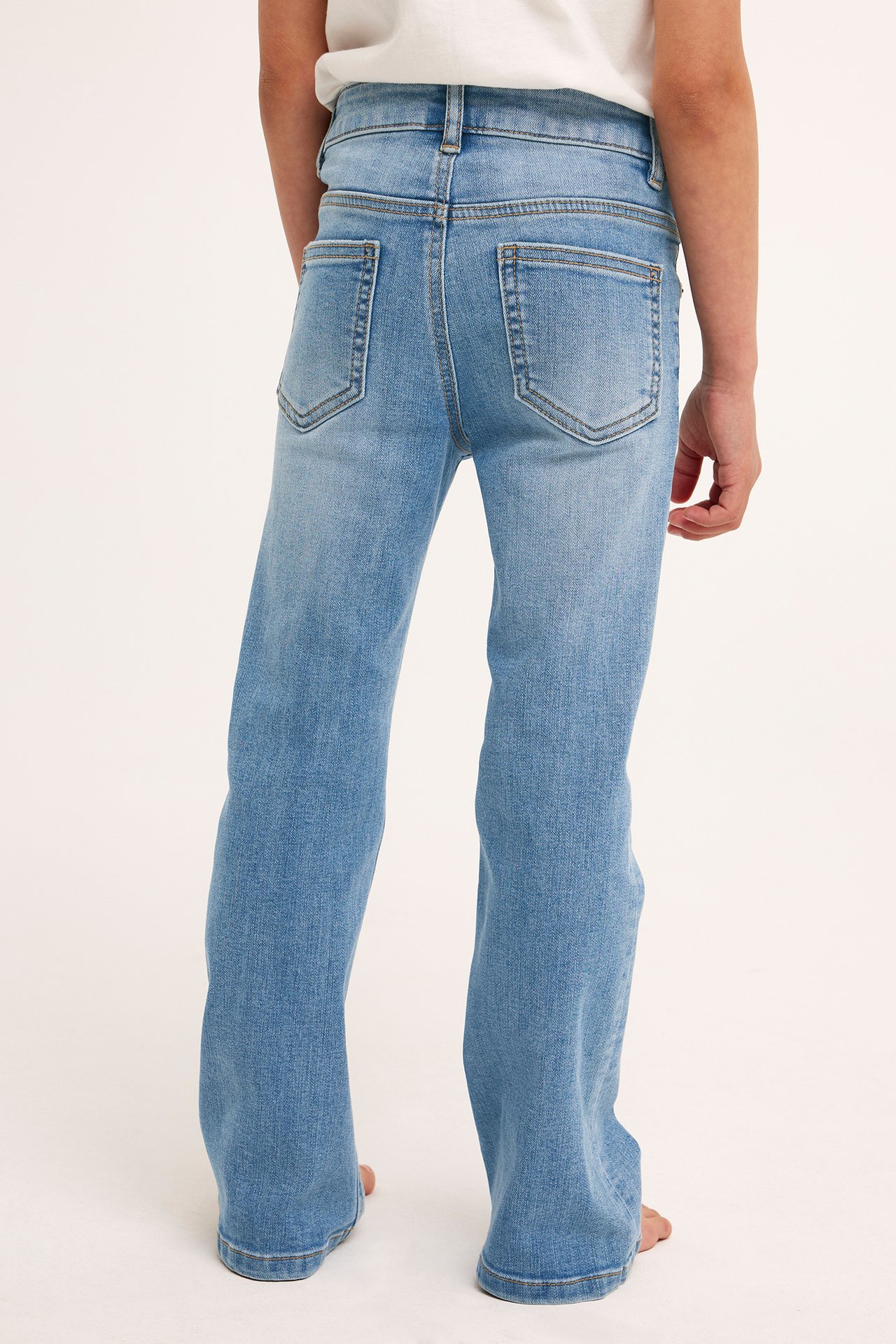 Bakifrån, ett barn i ljusblå bootcut jeans i denim med bakfickor och en vit t-shirt.