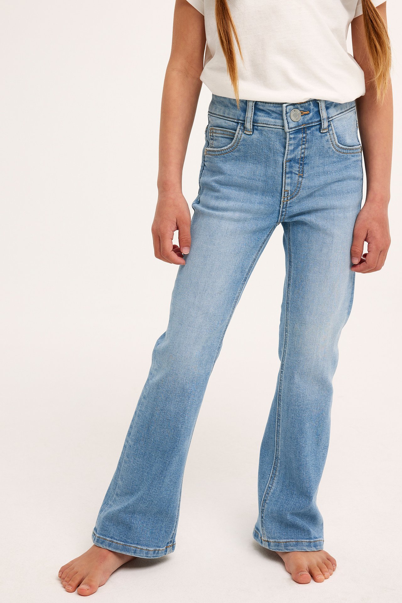 Framifrån, ett barn i ljusblå bootcut jeans i stretchdenim med tryckknapp och en vit t-shirt.