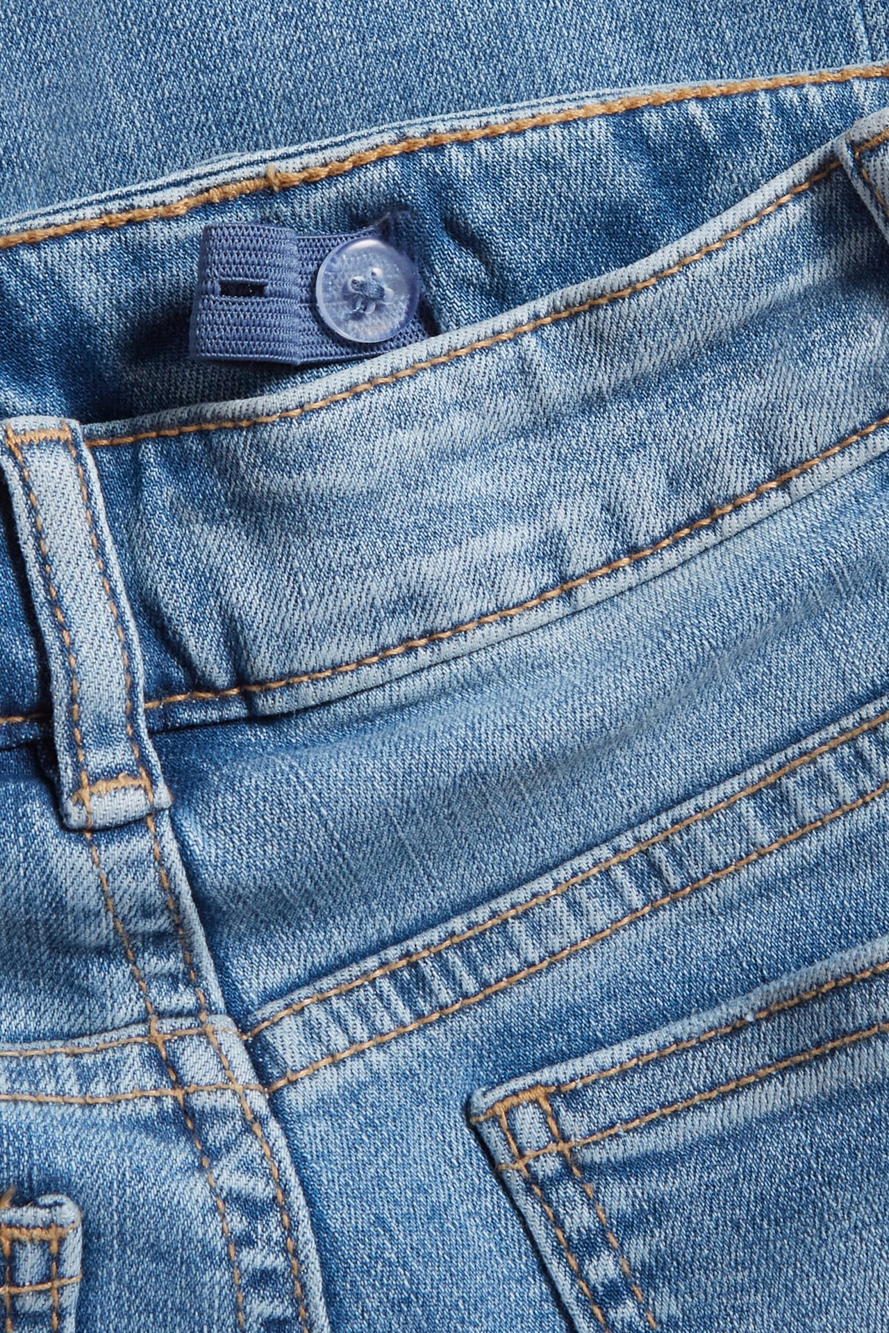 Närbild på barnens ljusblå bootcut jeans i denim, med justerbar resår och knapp i midjan.