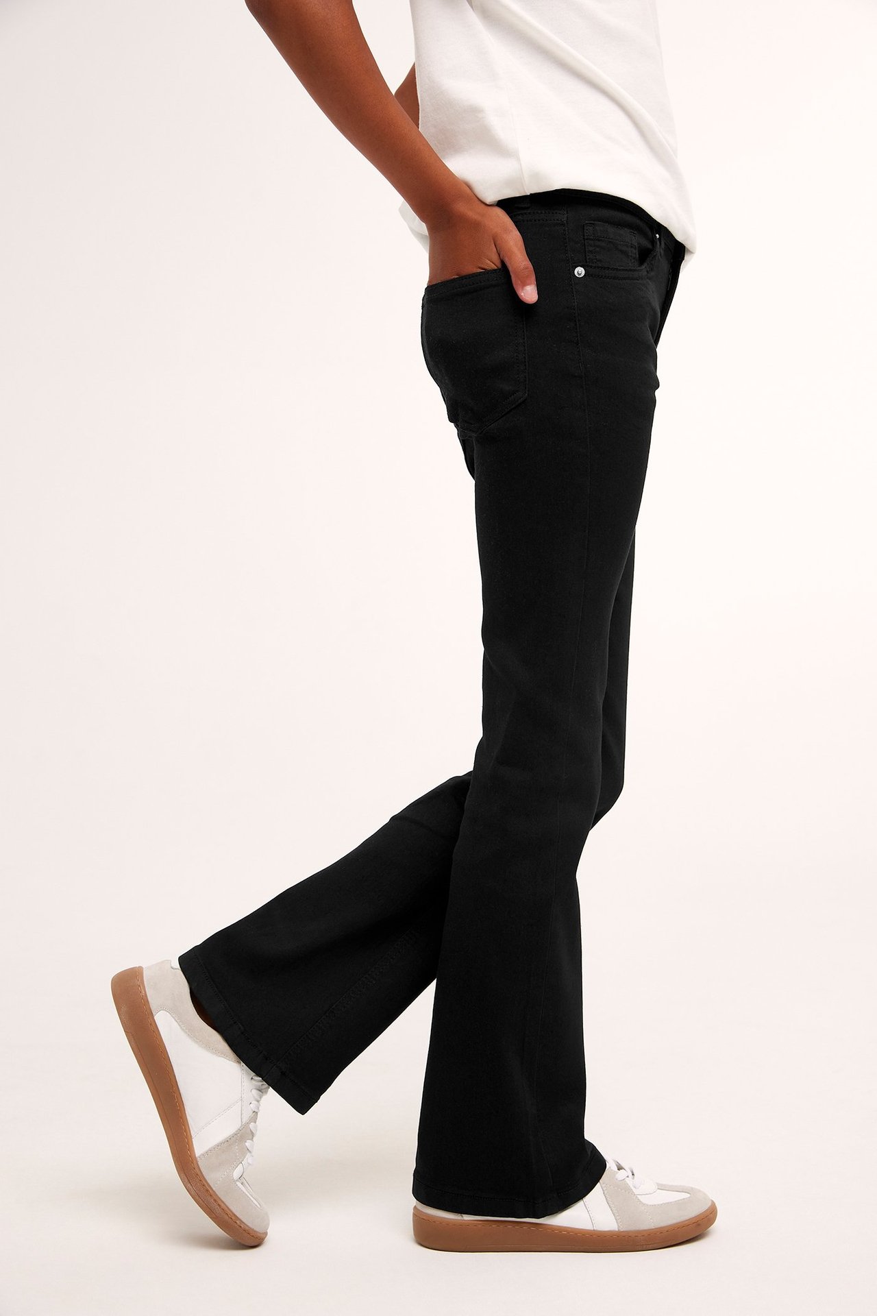 Sivukuva: Lapsi mustissa bootcut-farkuissa, valkoisessa t-paidassa ja valkoisissa-beigenvärisissä tennareissa.