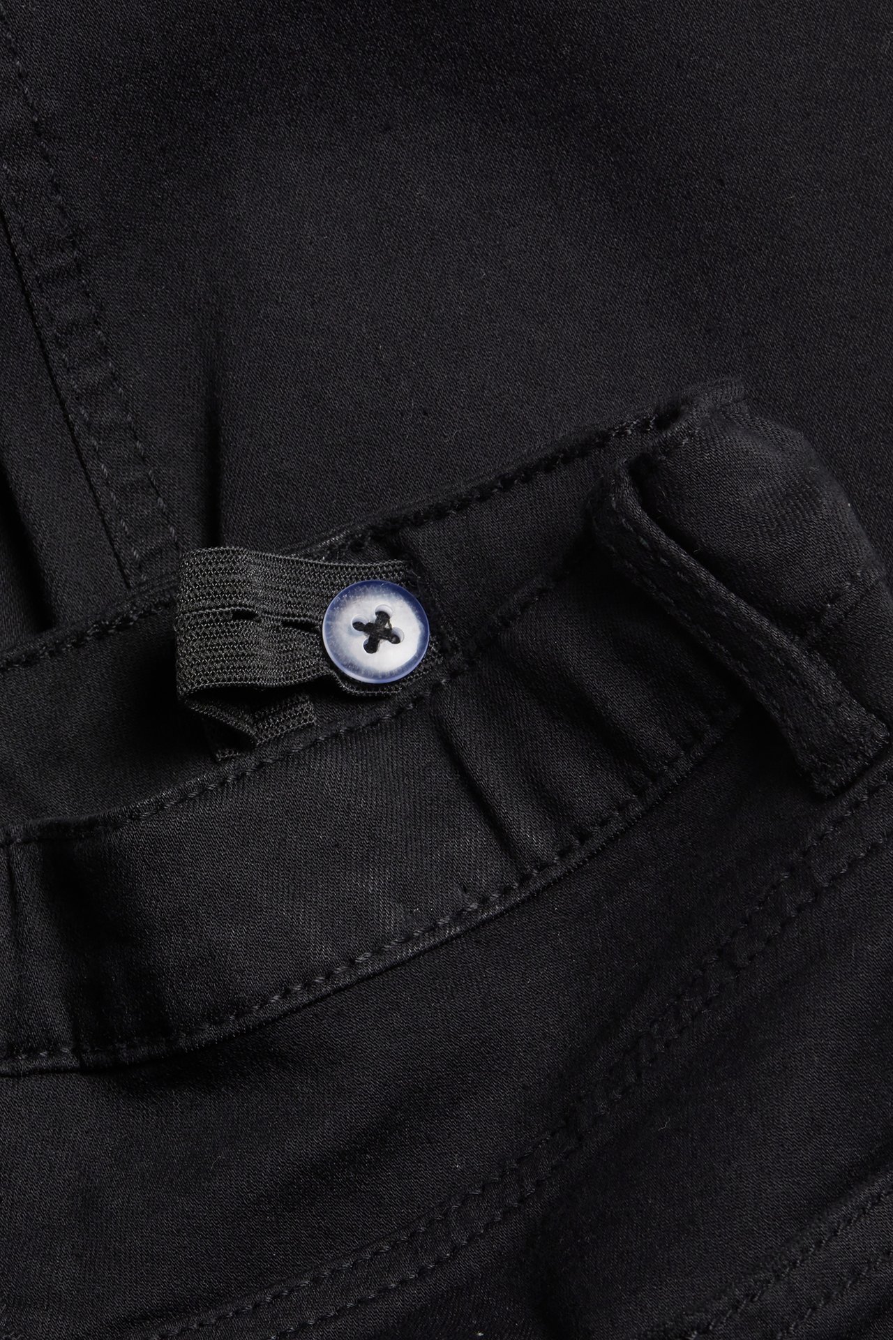 Lähikuva lasten mustista bootcut-farkuista, joissa säädettävä vyötärö ja sininen nappi.