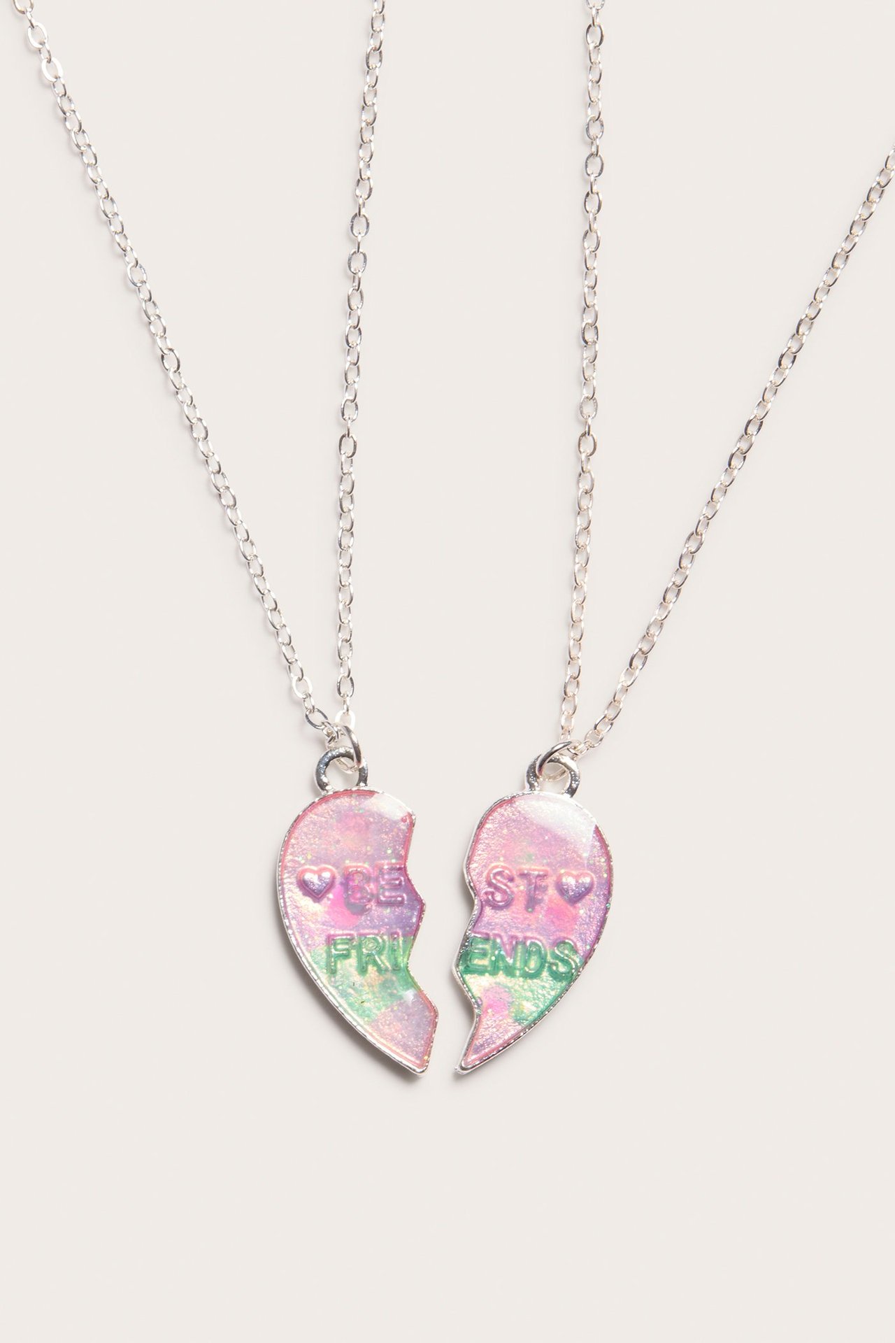 Zbliżenie dwóch srebrnych metalowych naszyjników BFF z opalizującymi połówkami serc, tworzącymi 'BEST FRIENDS'.