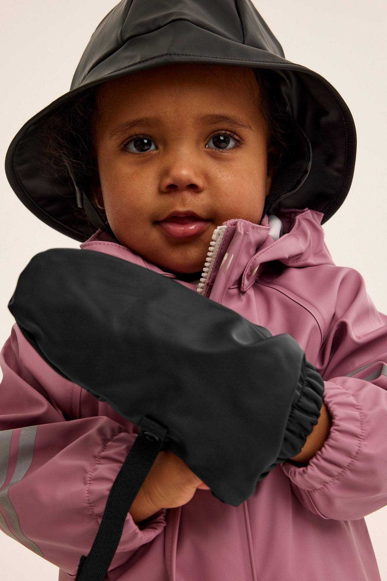Pieni tyttö vaaleanpunaisessa vedenpitävässä takissa ja mustissa fleece-mantelihanskoissa, etupuoli.