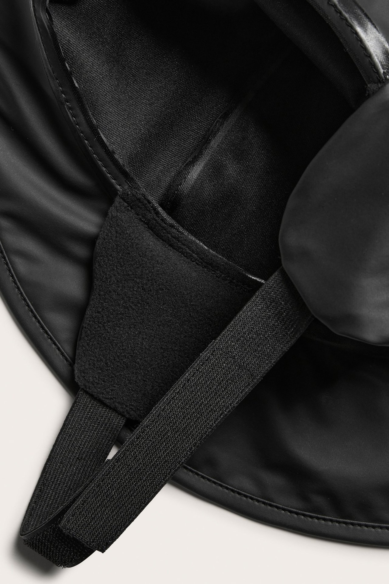 Zbliżenie na czarny kapelusz przeciwdeszczowy dla dziecka z szerokim rondem, polarową podszewką i elastycznym paskiem.