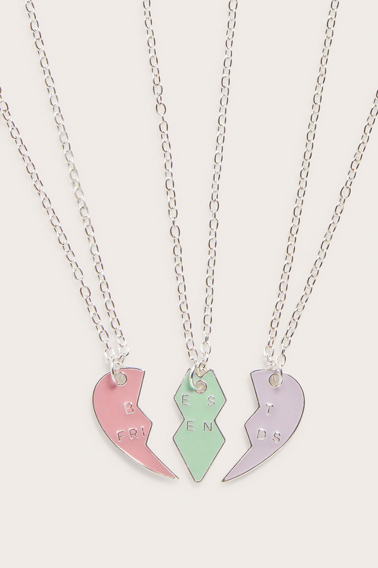 Zbliżenie na trzy srebrne naszyjniki BFF z różowymi, zielonymi i fioletowymi zawieszkami serca, tworzącymi 'BEST FRIENDS'.