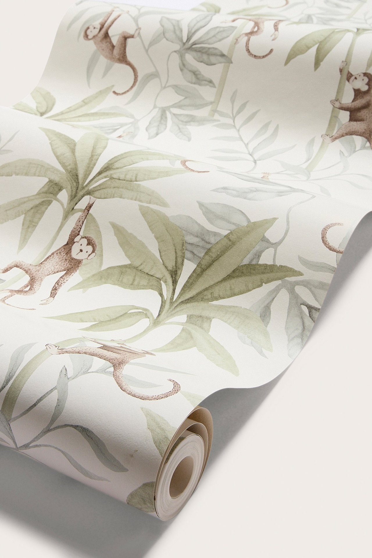 Närbild på en vit papperstapet i rulle med djungelmönster av apor och gröna blad.