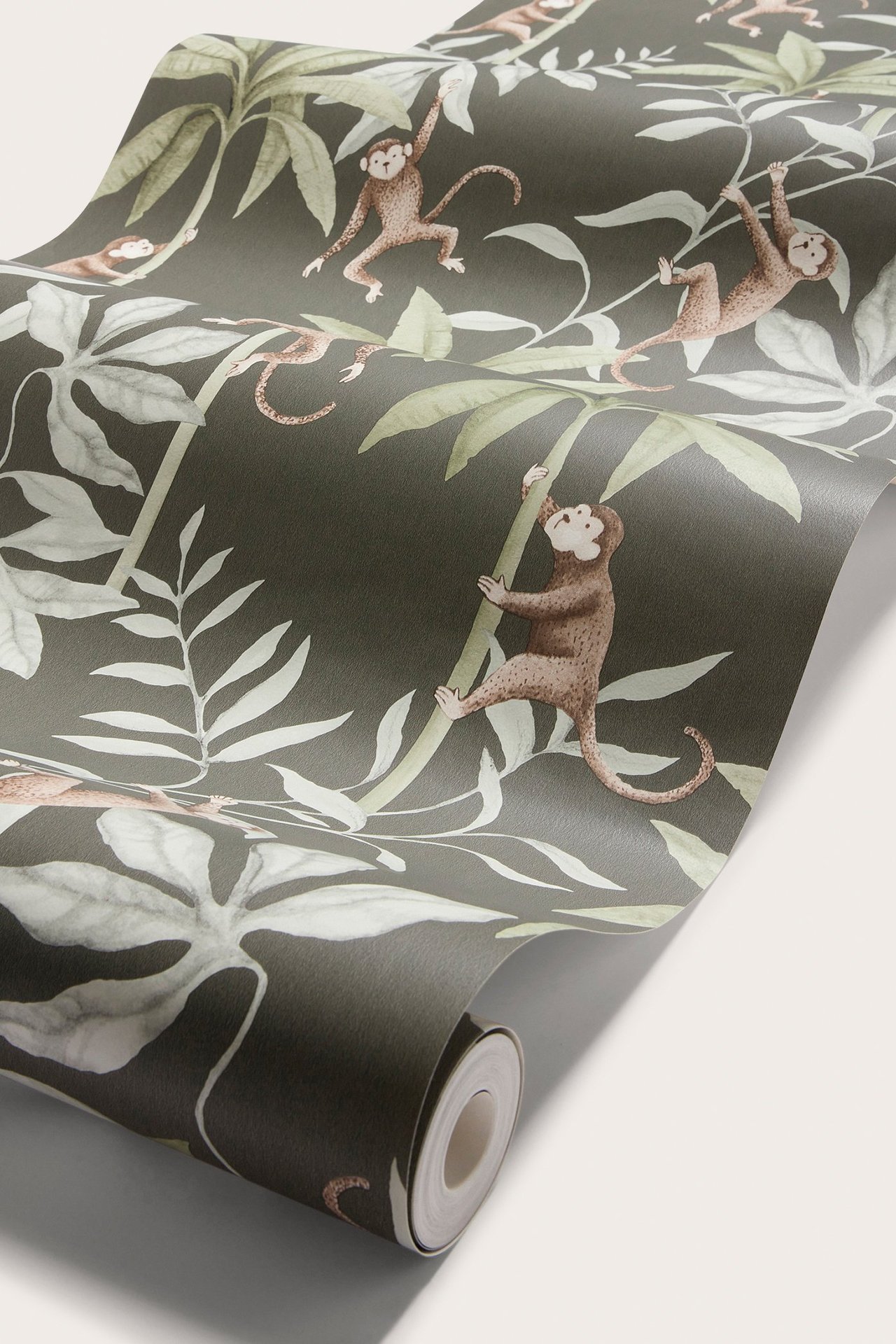 Zbliżenie na rolkę tapety z ciemnozielonym liściem i brązowym wzorem małp.