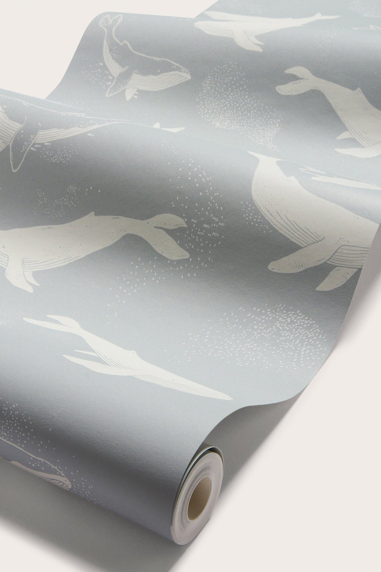 Närbild av en ljusblå tapetrulle med mönster av vita valar och små prickar.