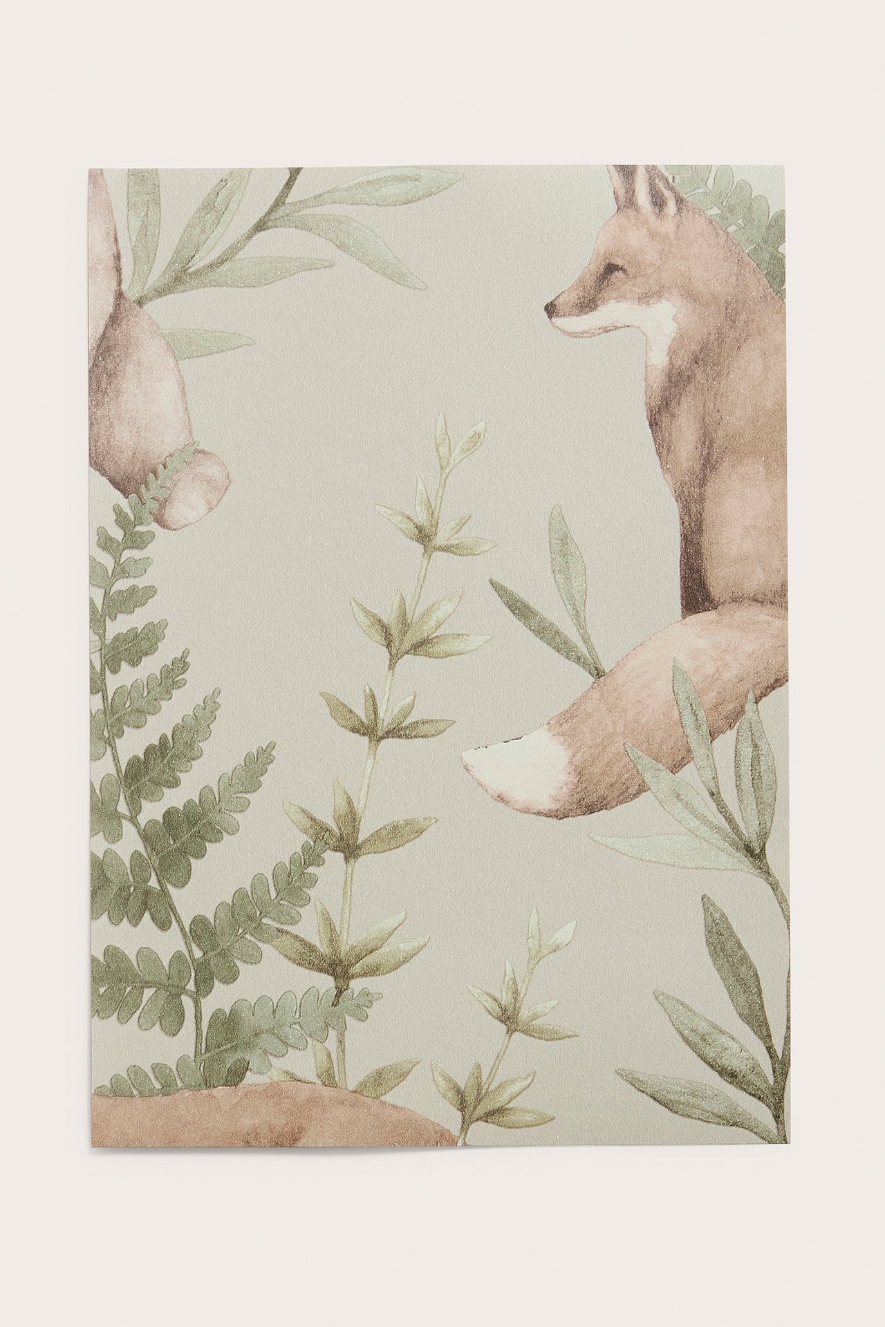 Närbild av ett beige non-woven tapetprov med mönster av räv, del av björn och gröna skogsväxter.