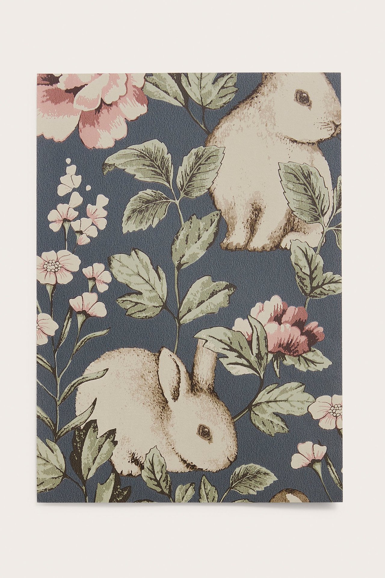 Nærbilde av en blå mønstret tapetprøve med hvite kaniner, grønne blader og rosa blomster.