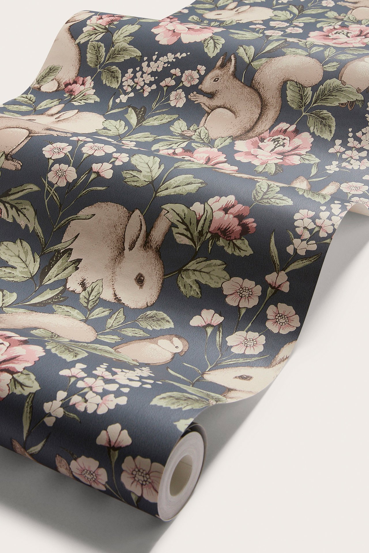 Närbild av blå mönstrad non-woven tapet med beiga kaniner, ekorrar, fåglar och rosa blommor.