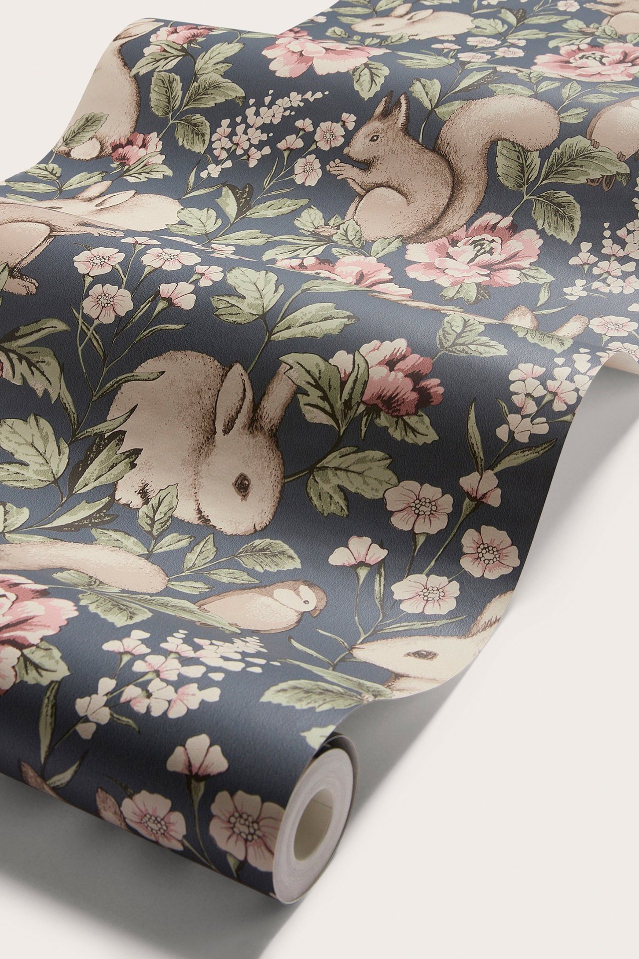 Närbild av blå mönstrad non-woven tapet med beiga kaniner, ekorrar, fåglar och rosa blommor.