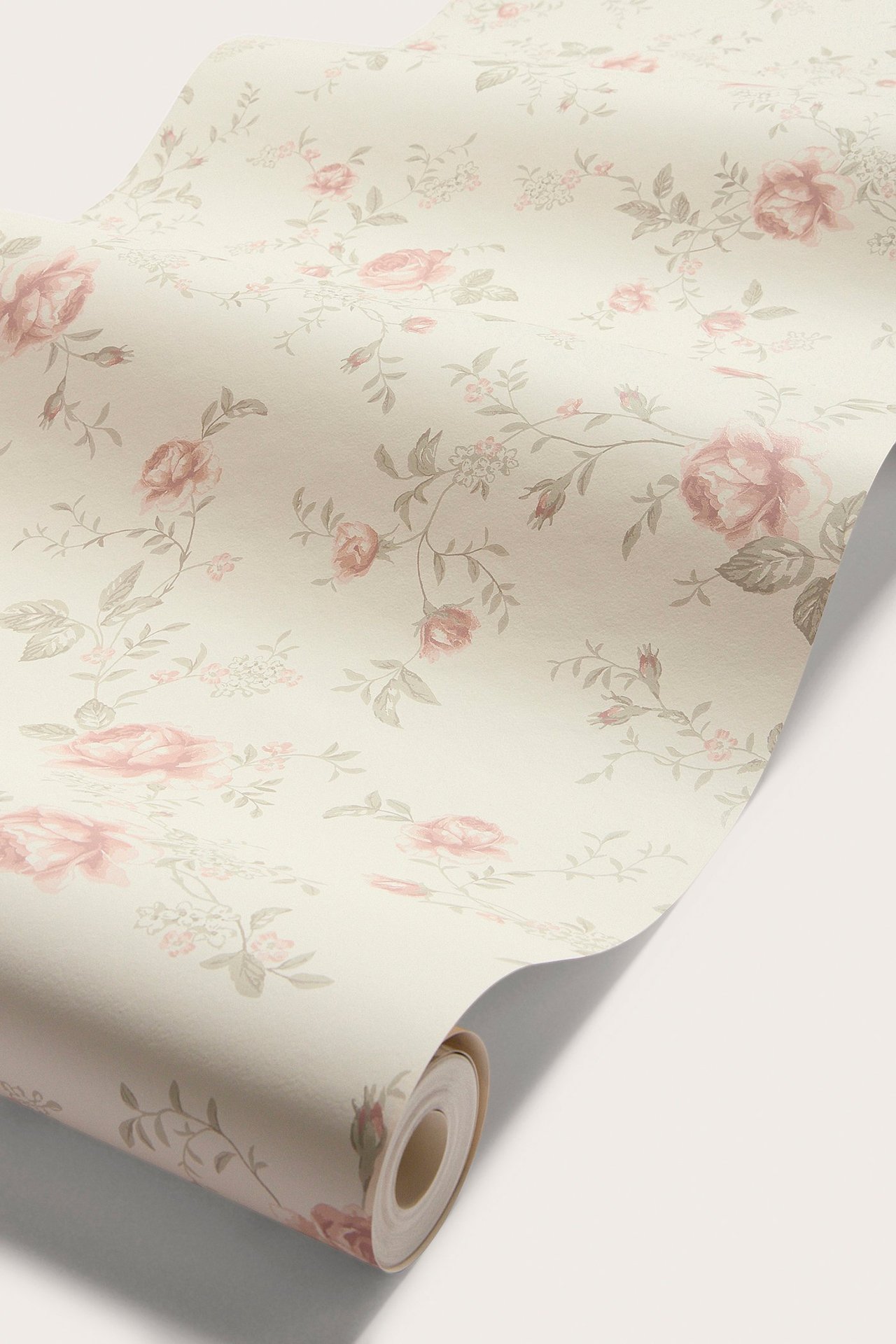 Zbliżenie częściowo rozwiniętej beżowej tapety w różowe róże i szarobrązowe liście.