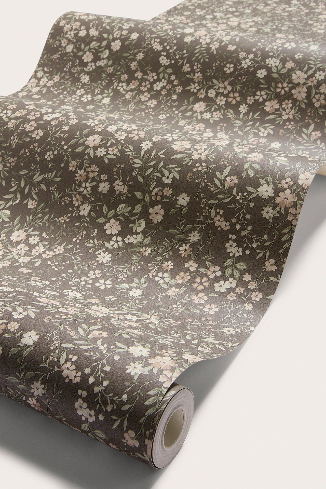 Kuvakulma ruskeasta paperitapetista, jossa pieni vaalea kukkakuvio, aukeaa rullana.