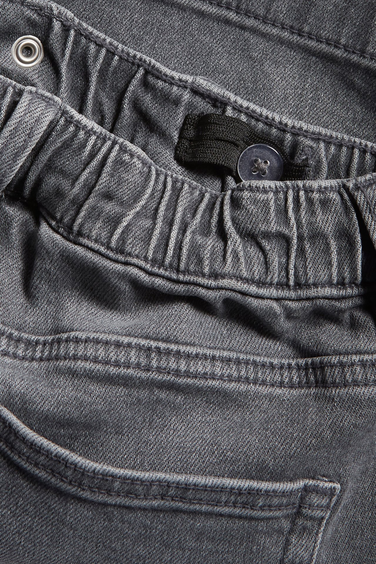 Närbild på ljusgråa jeansshorts för barn med resår i midjan, tryckknapp och reglerbar resår inuti.