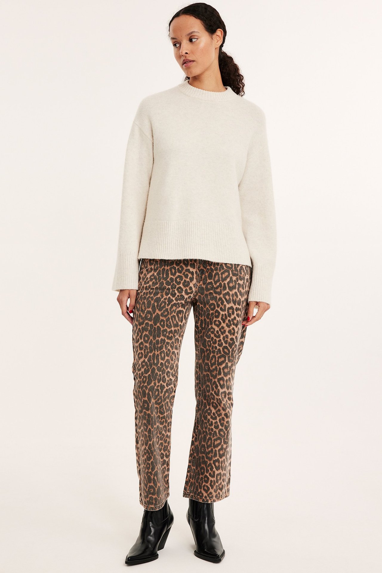 Edestä kuvattu nainen yllään luonnonvalkoinen meleerattu neulepusero, leopardikuvioiset housut ja mustat nilkkurit.