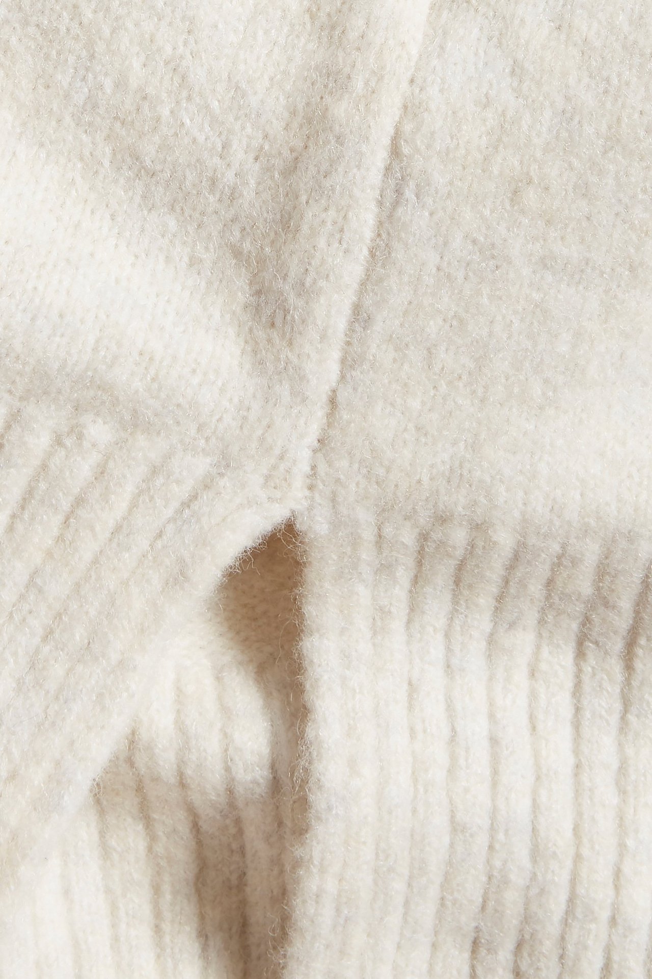 Zbliżenie na dzianinowy sweter w kolorze złamanej bieli, melanżowy, z widocznym ściągaczem.