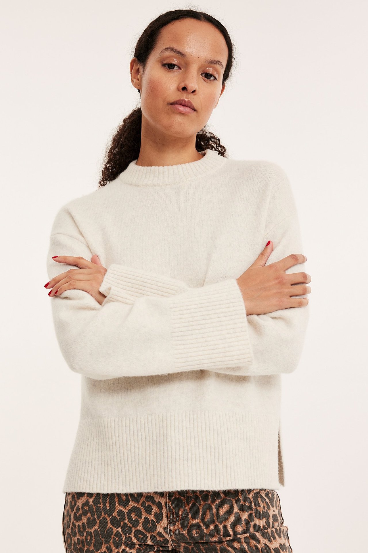 Edestä kuvattu nainen yllään luonnonvalkoinen meleerattu neulepusero ja ruskeat leopardikuvioiset housut.