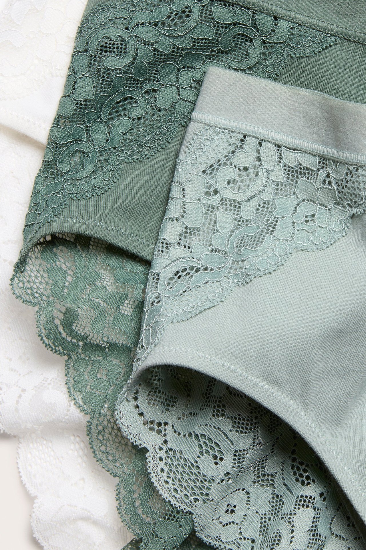 Zbliżenie jasnozielonych majtek z koronką, obok ciemnozielonych i białych majtek z koronką.