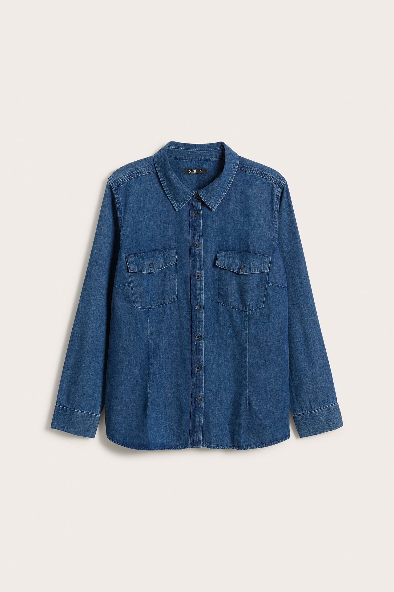 Frontvisning av en ensfarget denimblå langermet bomullsskjorte med krage, knappelukking og to klafflommer.