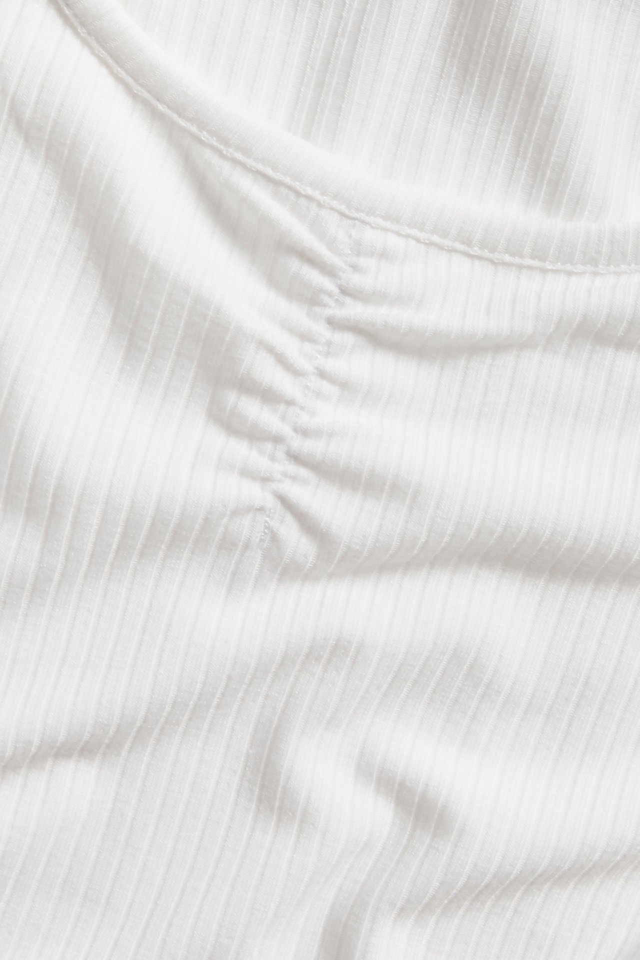Närbild av en offwhite ribbad pyjamastopp med rynkdetalj framtill.