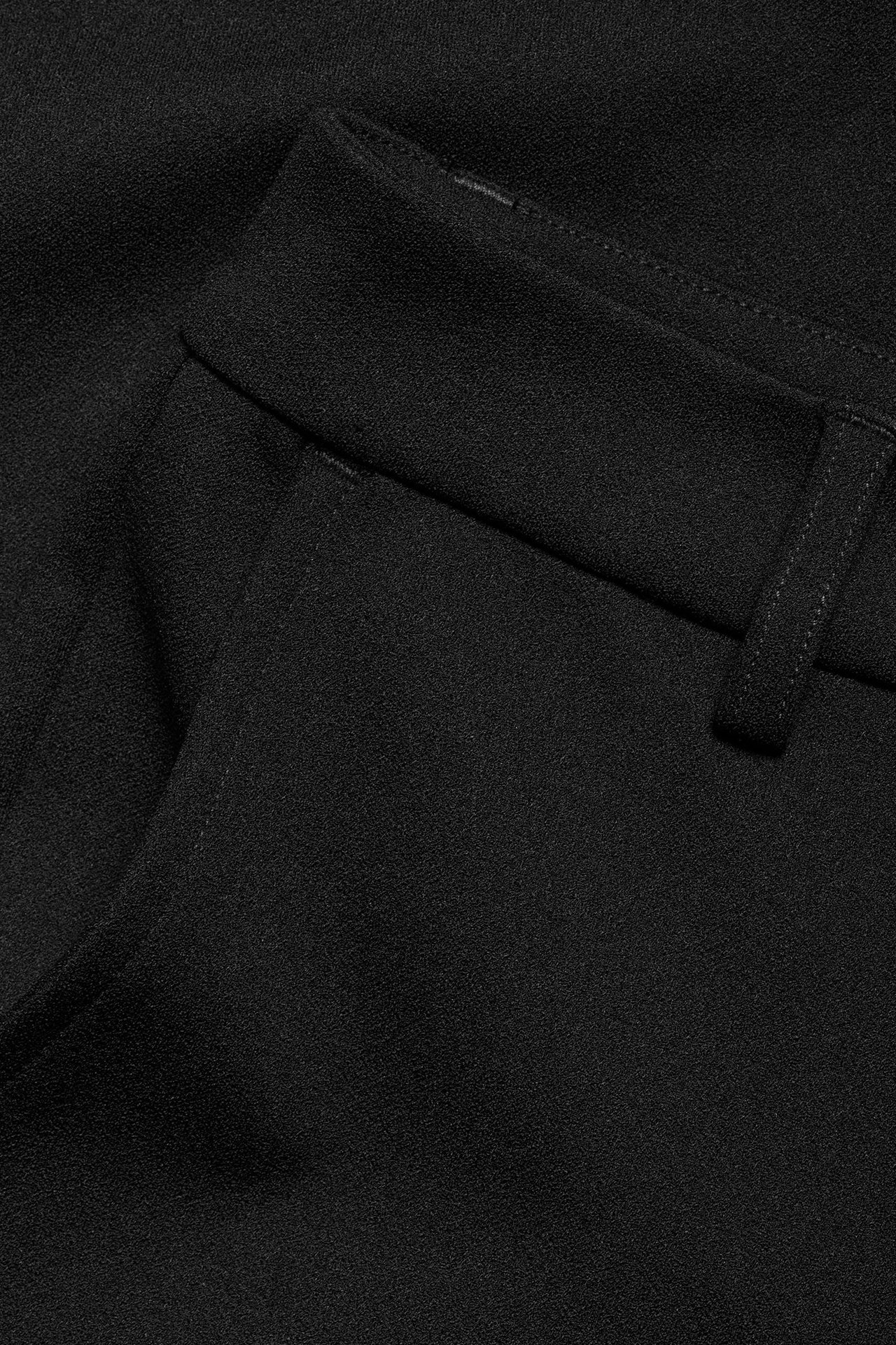 Zbliżenie czarnych spodni garniturowych z dzianiny, pokazujące pas, szlufkę i otwór kieszeni.