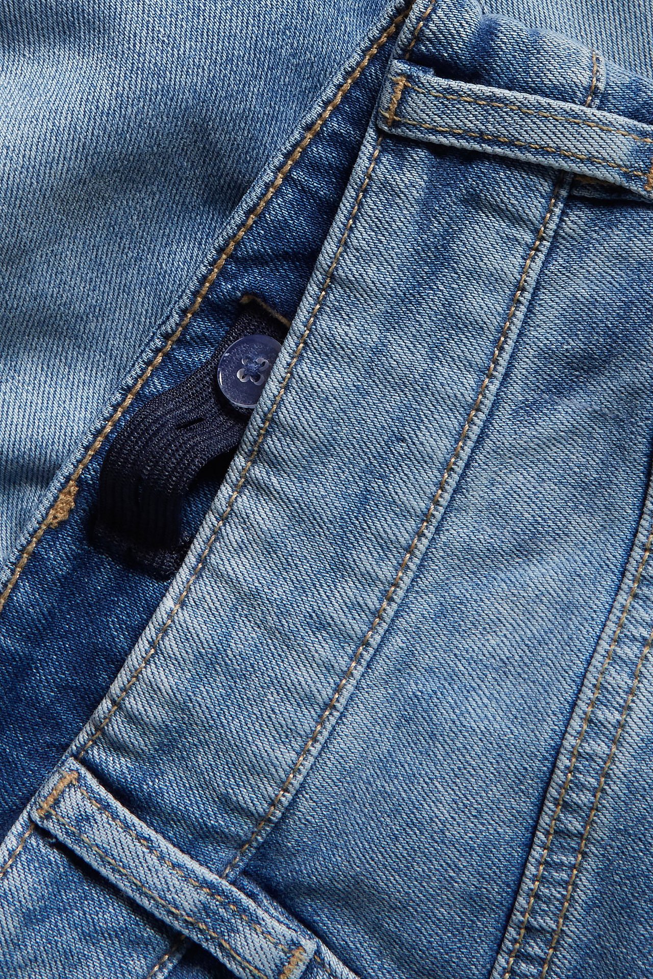 Zbliżenie na jasnoniebieskie luźne jeansy denim z regulowaną gumką w pasie i guzikiem.