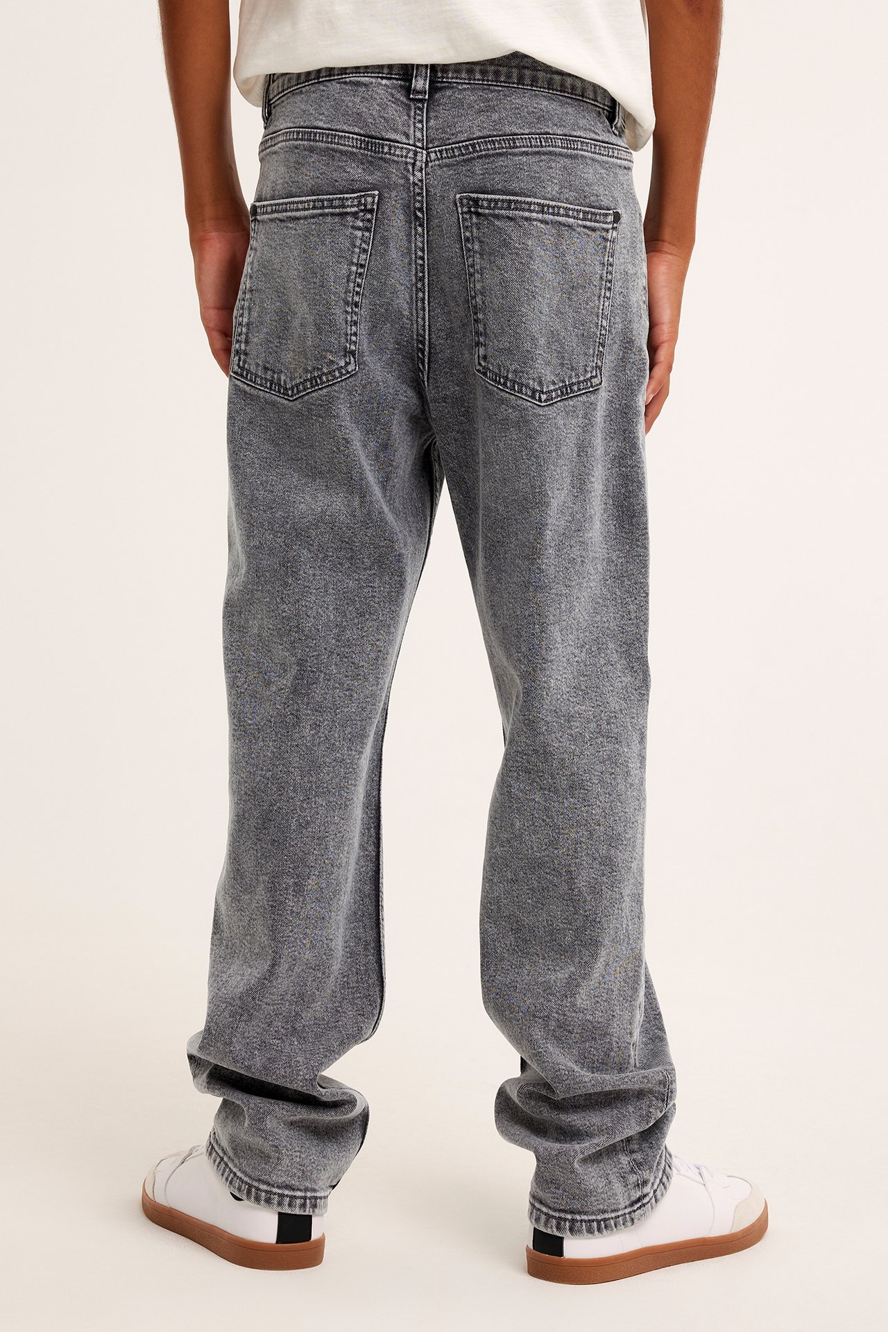 Bakifrån, ett barn i grå loose-fit denimjeans, en vit t-shirt och vita sneakers.