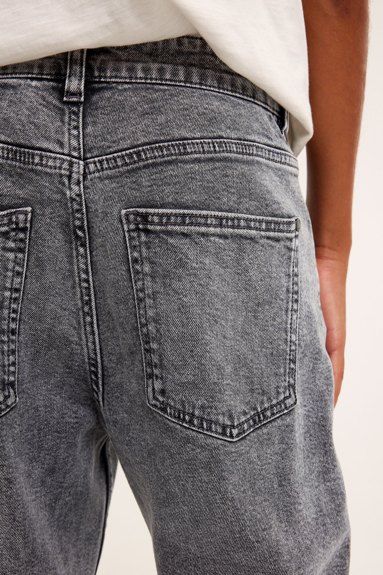Närbild bakifrån på ett barn i gråa lösa jeans med bakfickor och en vit t-shirt.
