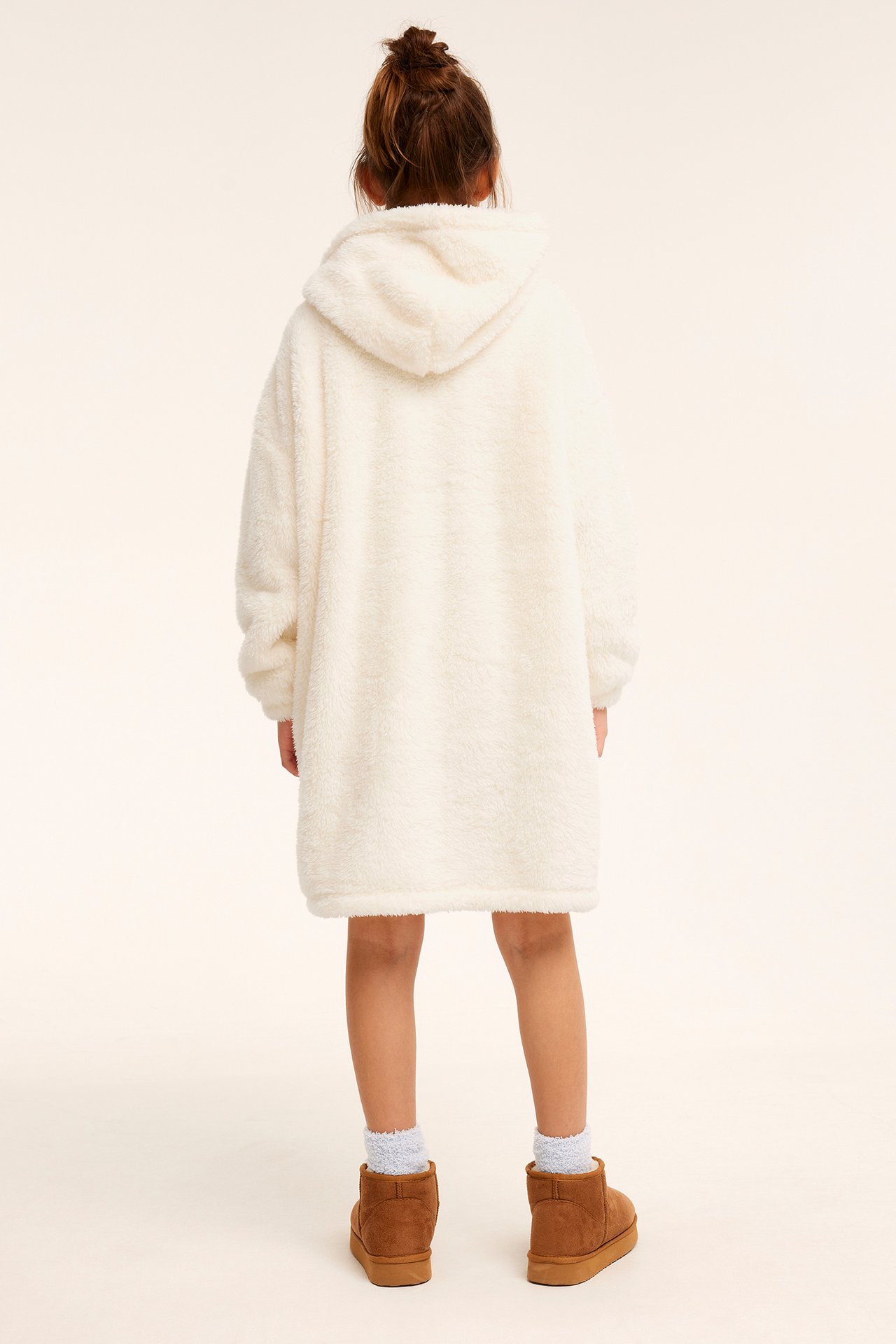 Bakifrån: ett barn i en offwhite oversized fleecehoodie, ljusblå strumpor och bruna ankelboots.