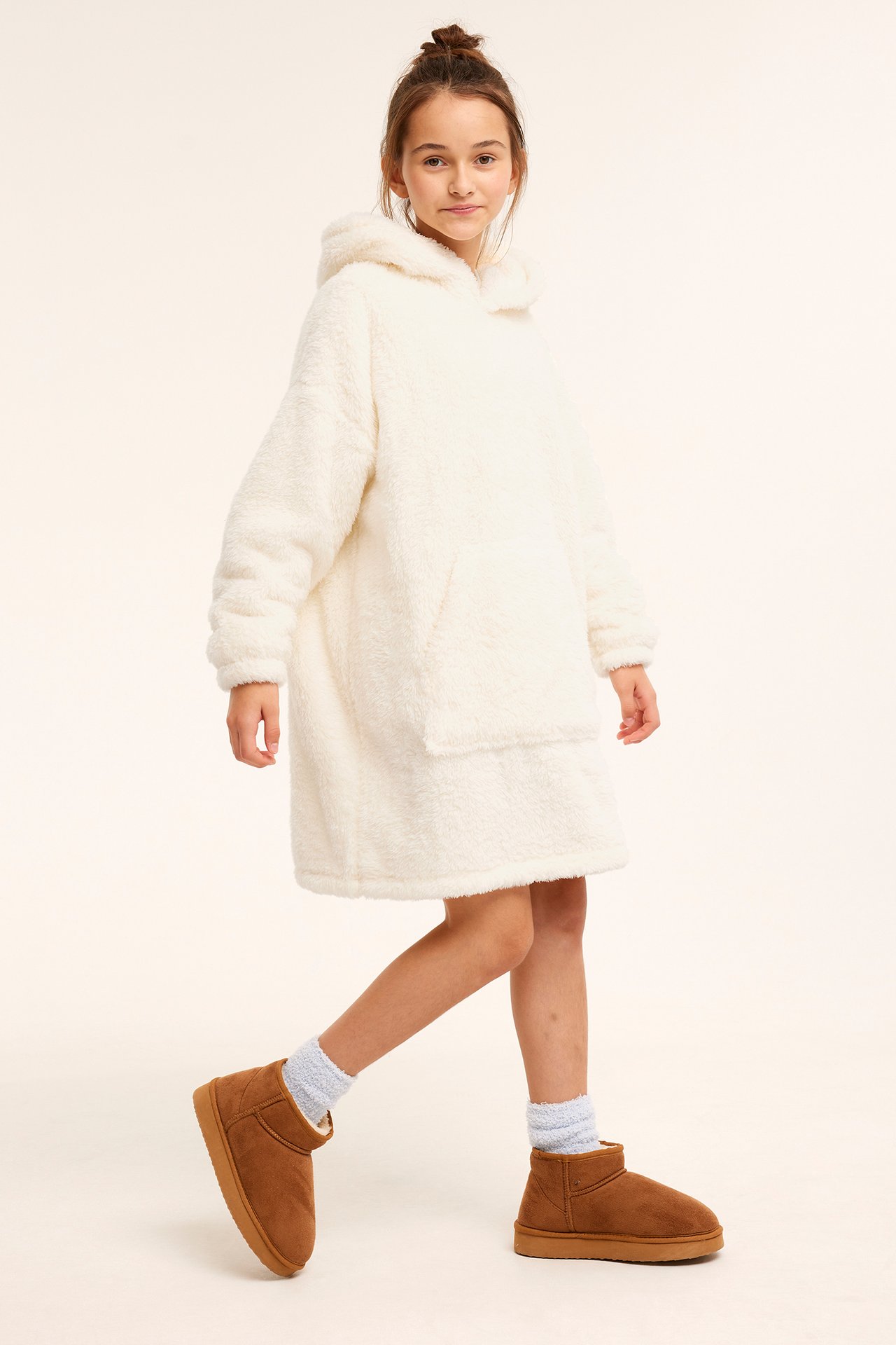 Framifrån, ett barn i oversized off-white fleecehoodie, ljusblå fluffiga strumpor och bruna ankelboots.