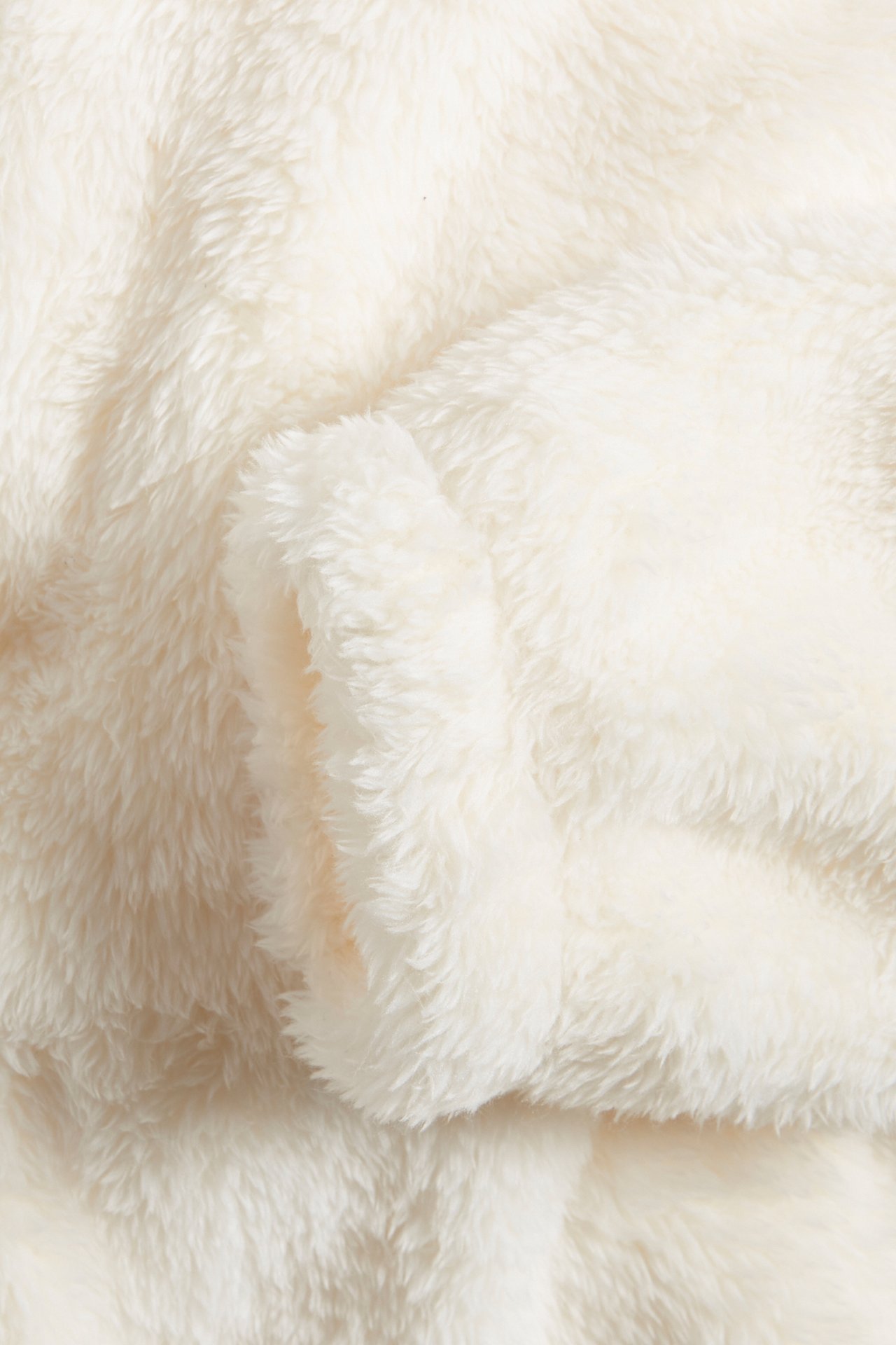 Närbild av en offwhite, enfärgad fleecehoodie, som visar den mjuka texturen och en vikt mudd.