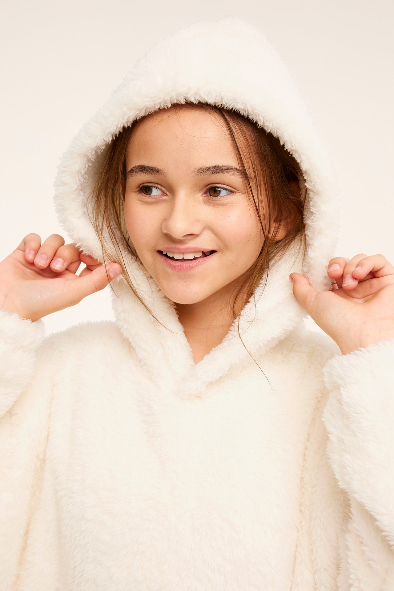 Närbild framifrån på ett barn som bär en oversized offwhite fleecehoodie och drar i huvan.