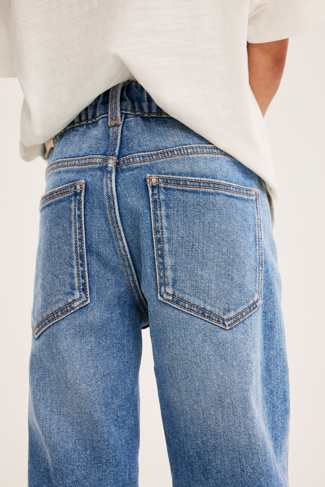 Widok z tyłu dziecka w jasnoniebieskich, luźnych dżinsach z denimu z elastyczną talią i jasnym t-shirtem.