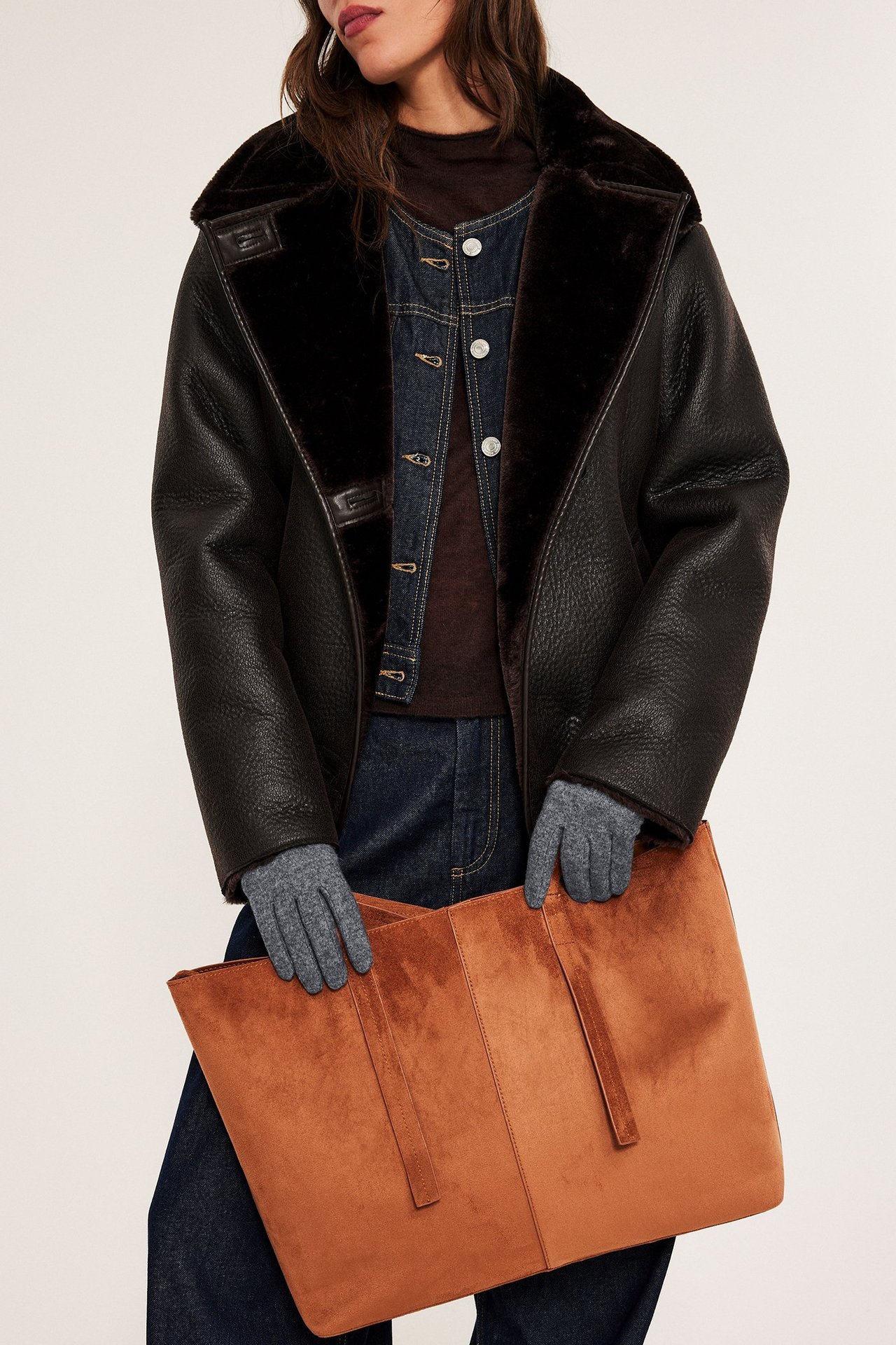 Szare melange rękawiczki z mieszanki wełny, kobieta w jeansowej kurtce i ciemnych ubraniach.