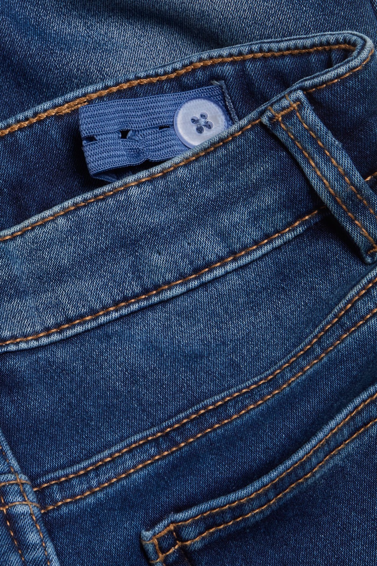 Zbliżenie na niebieskie dżinsy slim jogger denim z regulowaną gumką w pasie i białym guzikiem.