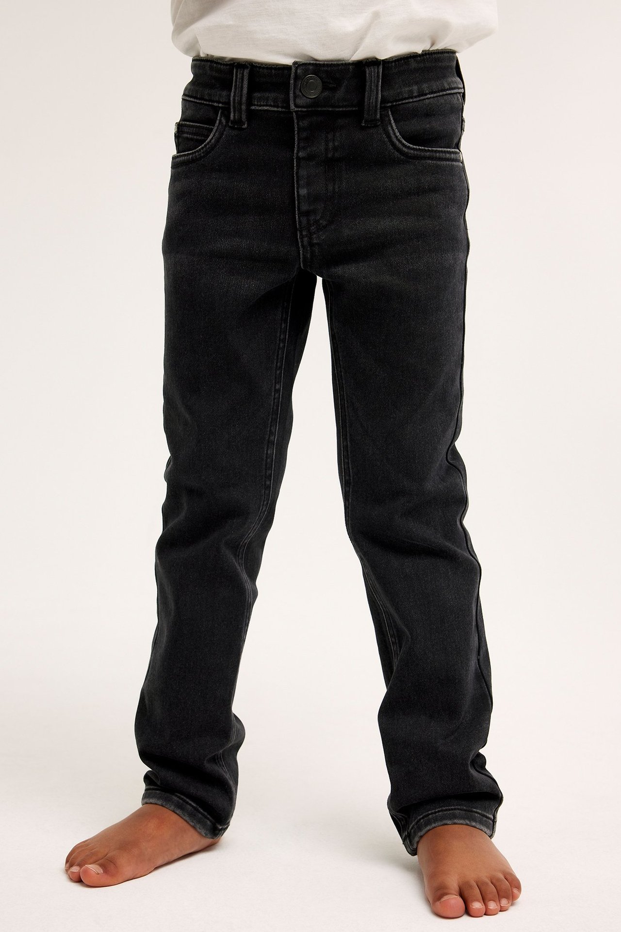Frontvy av ett barn i svarta slim-fit joggerjeans och en vit t-shirt.