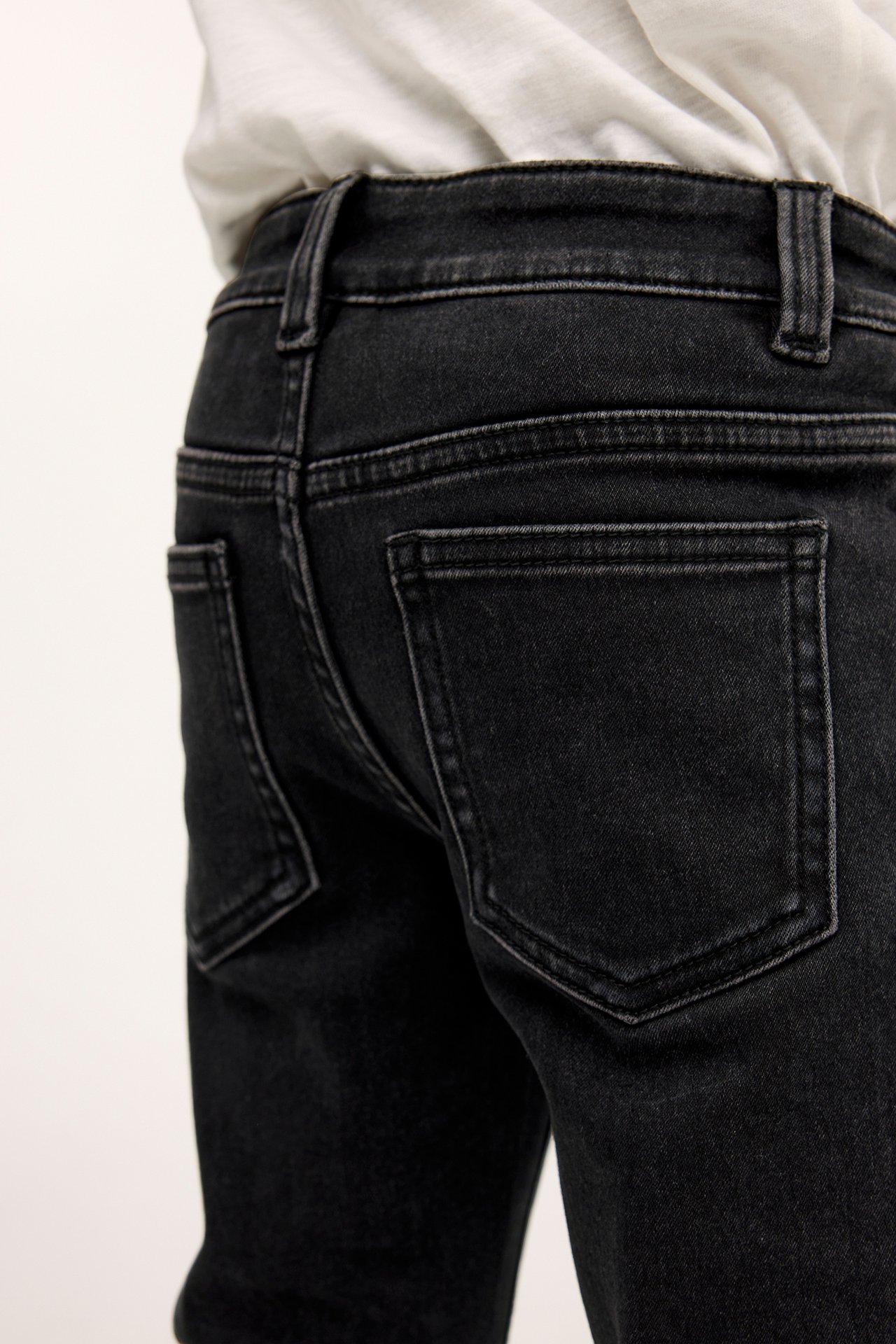 Lapsi takaa, yllään mustat slim jogger denim -farkut ja valkoinen t-paita.