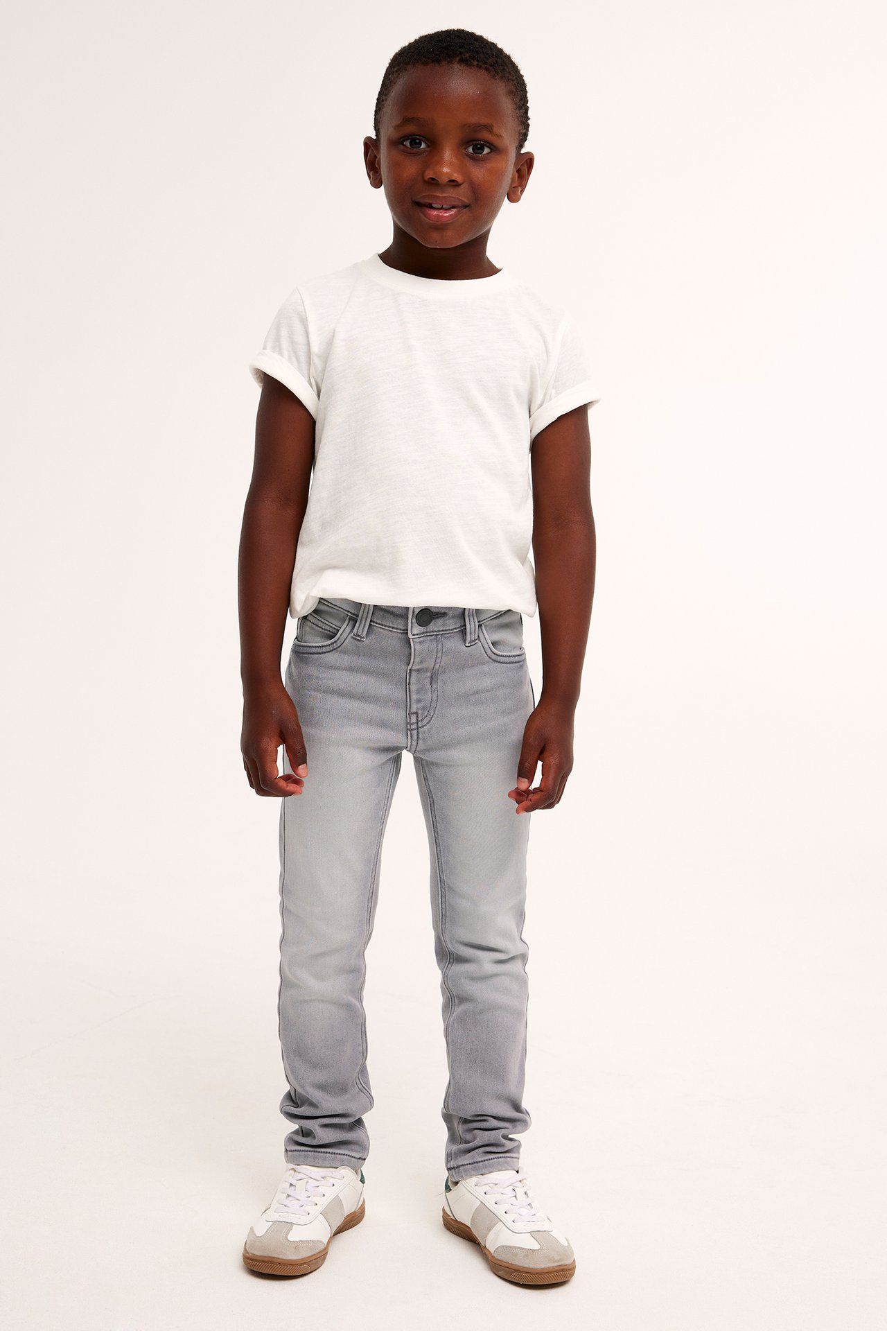 Frontvy av ett barn i gråa slim joggerdenim jeans, en vit t-shirt och vita sneakers.
