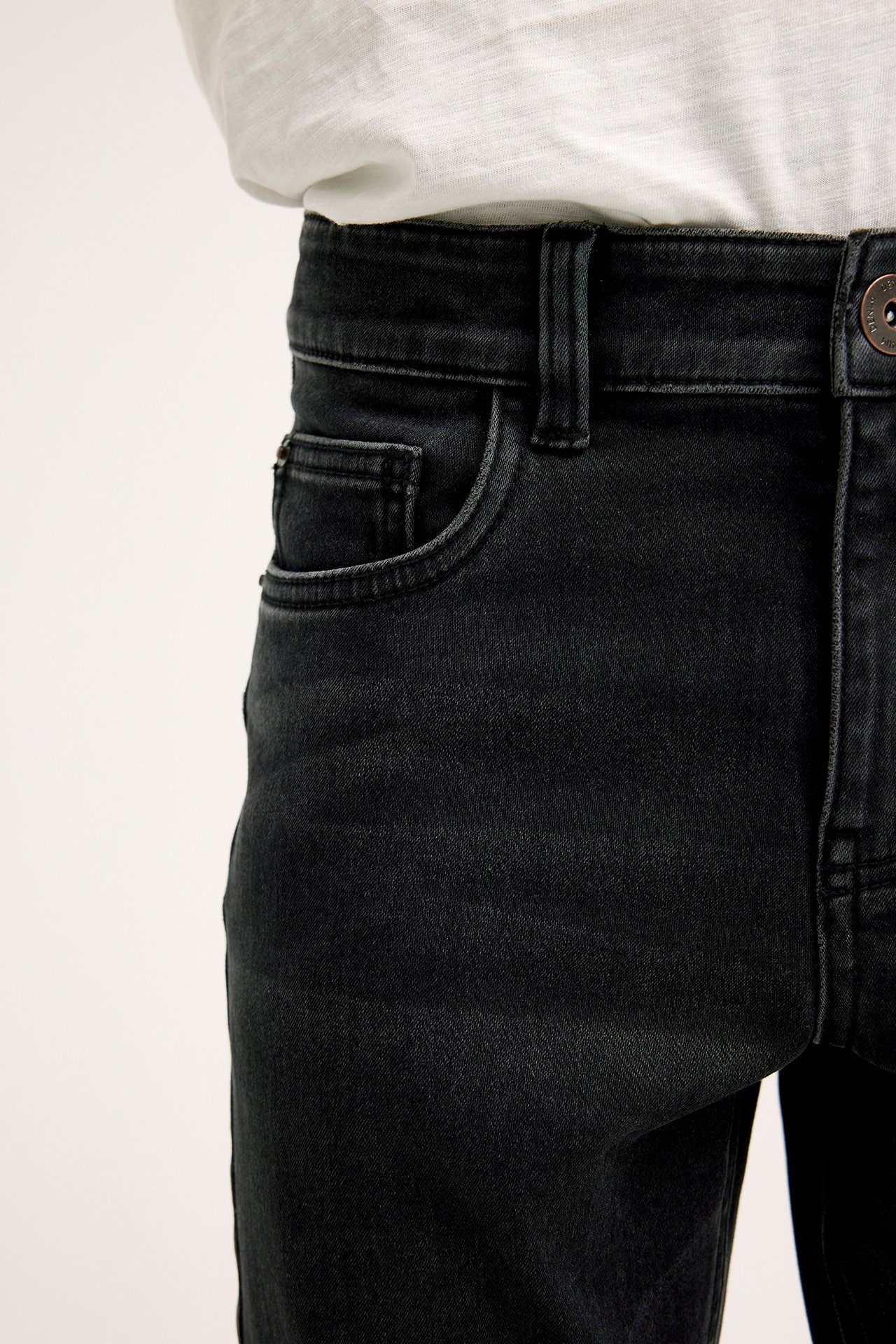 Närbild på barns svarta slim-fit jogger denim jeans med fem fickor, stylade med en vit t-shirt.