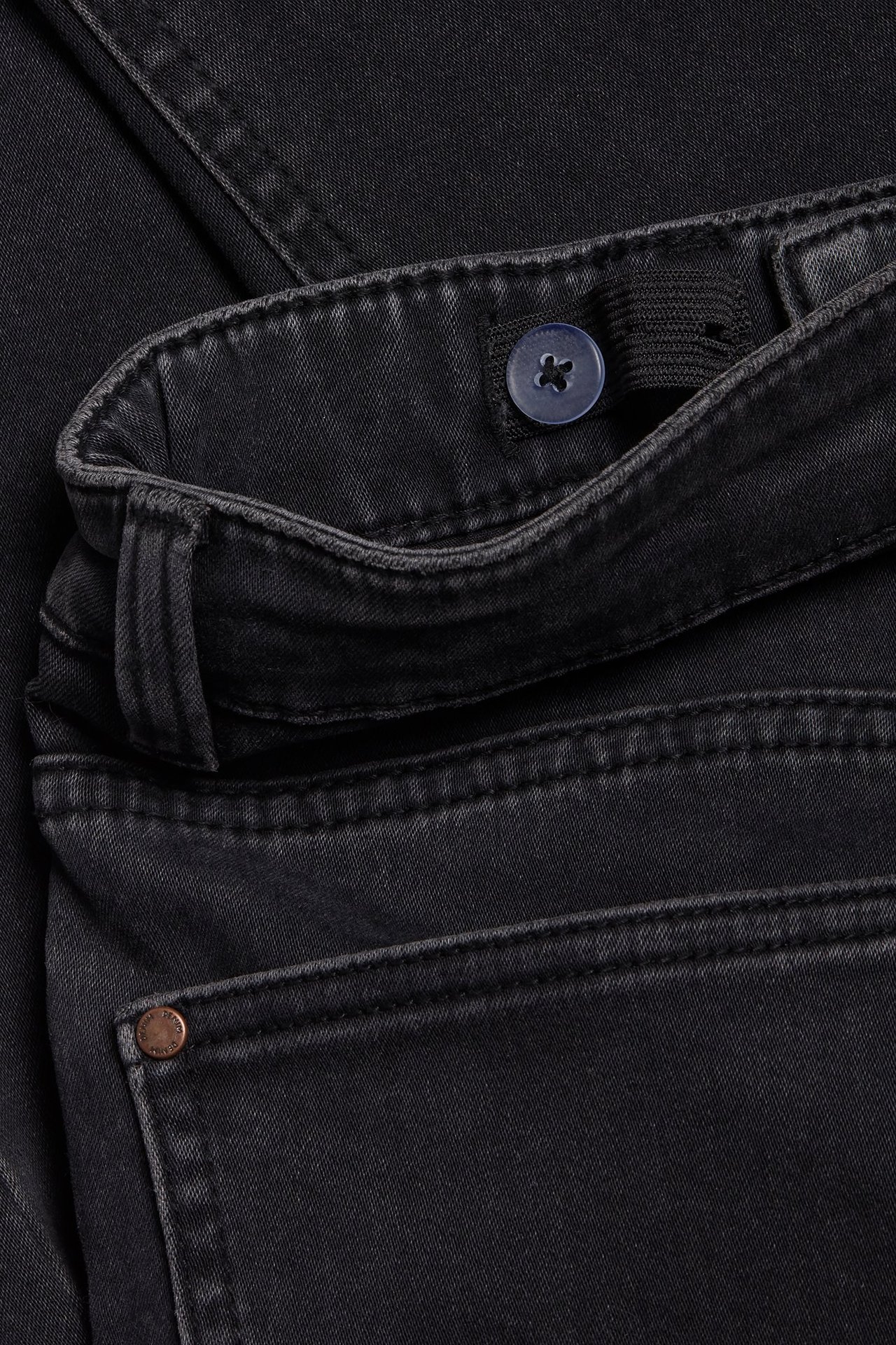 Zbliżenie czarnych dżinsów slim z jogger denimu z regulowaną talią i niebieskim guzikiem.