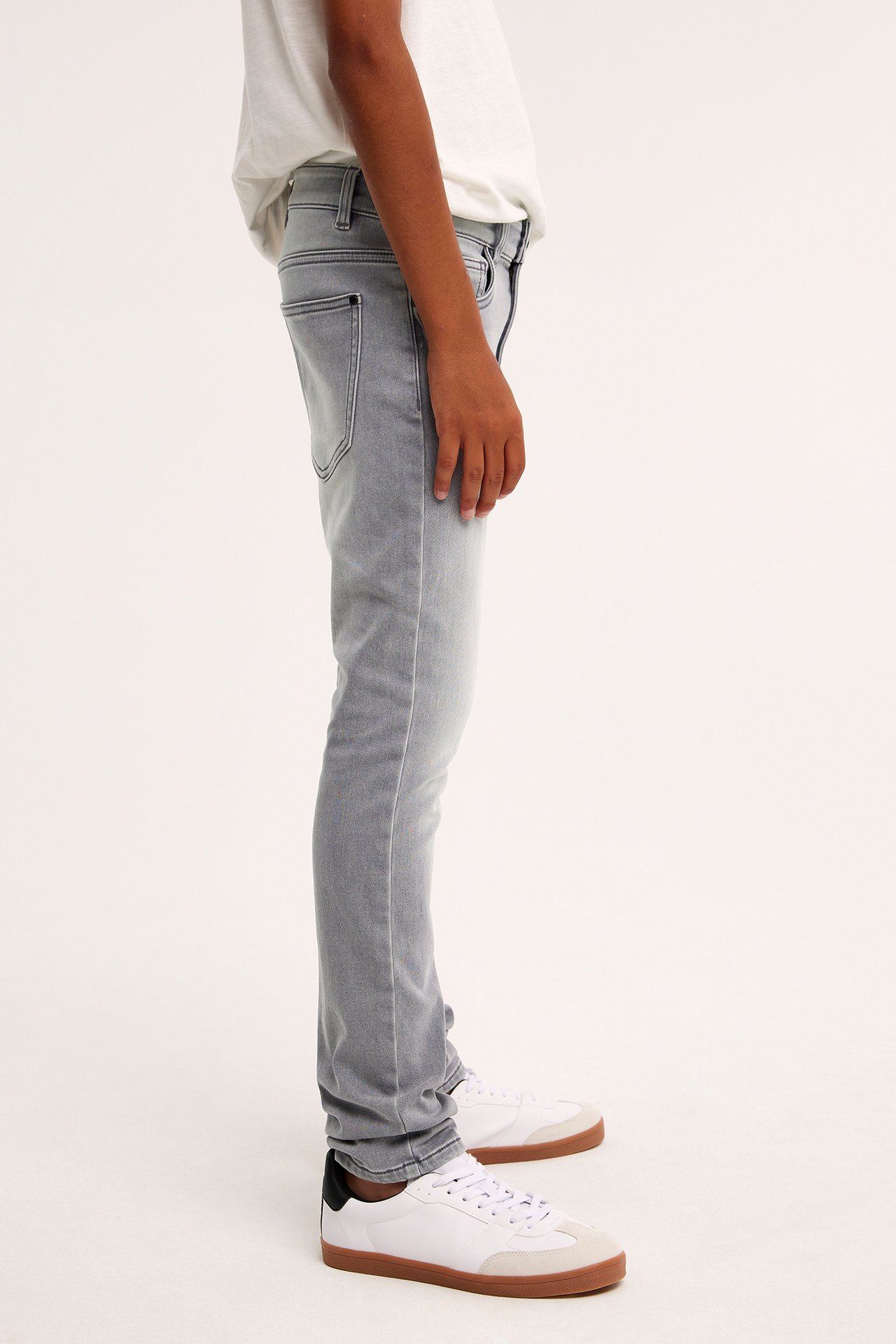 Sidovy av ett barn i gråa slim jogger denim jeans, en vit t-shirt och vita sneakers.