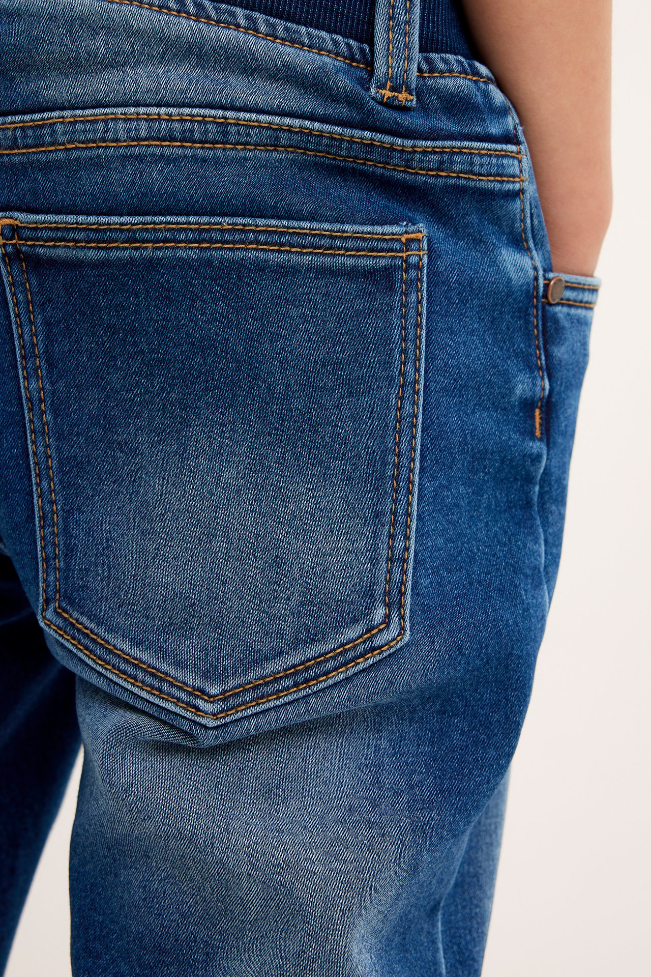 Närbild bakifrån på mörkblå joggerjeans för barn med orange sömmar och bakficka.