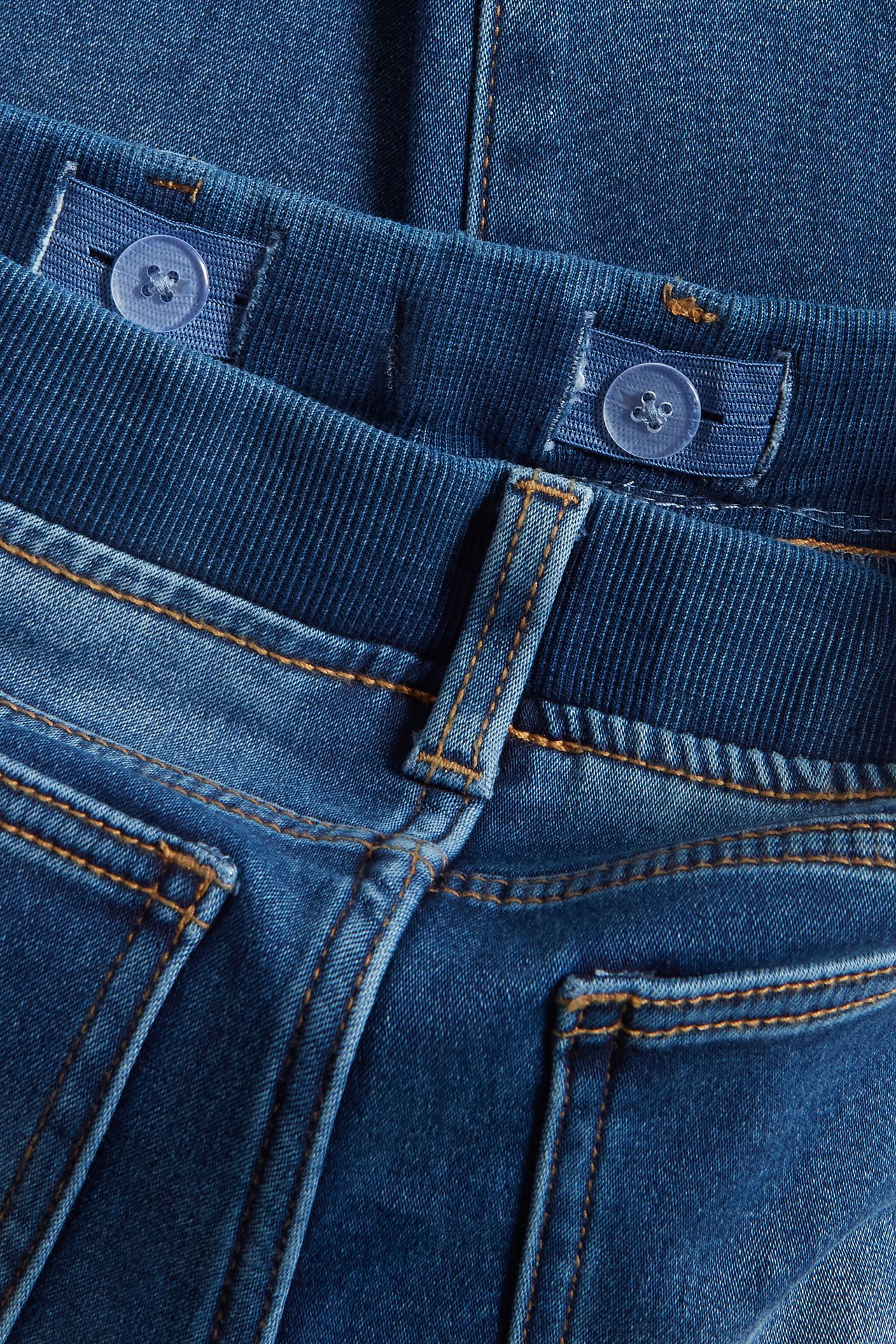 Närbild på barnens mörkblå joggerjeans med ribbad, justerbar midja och orange sömmar.