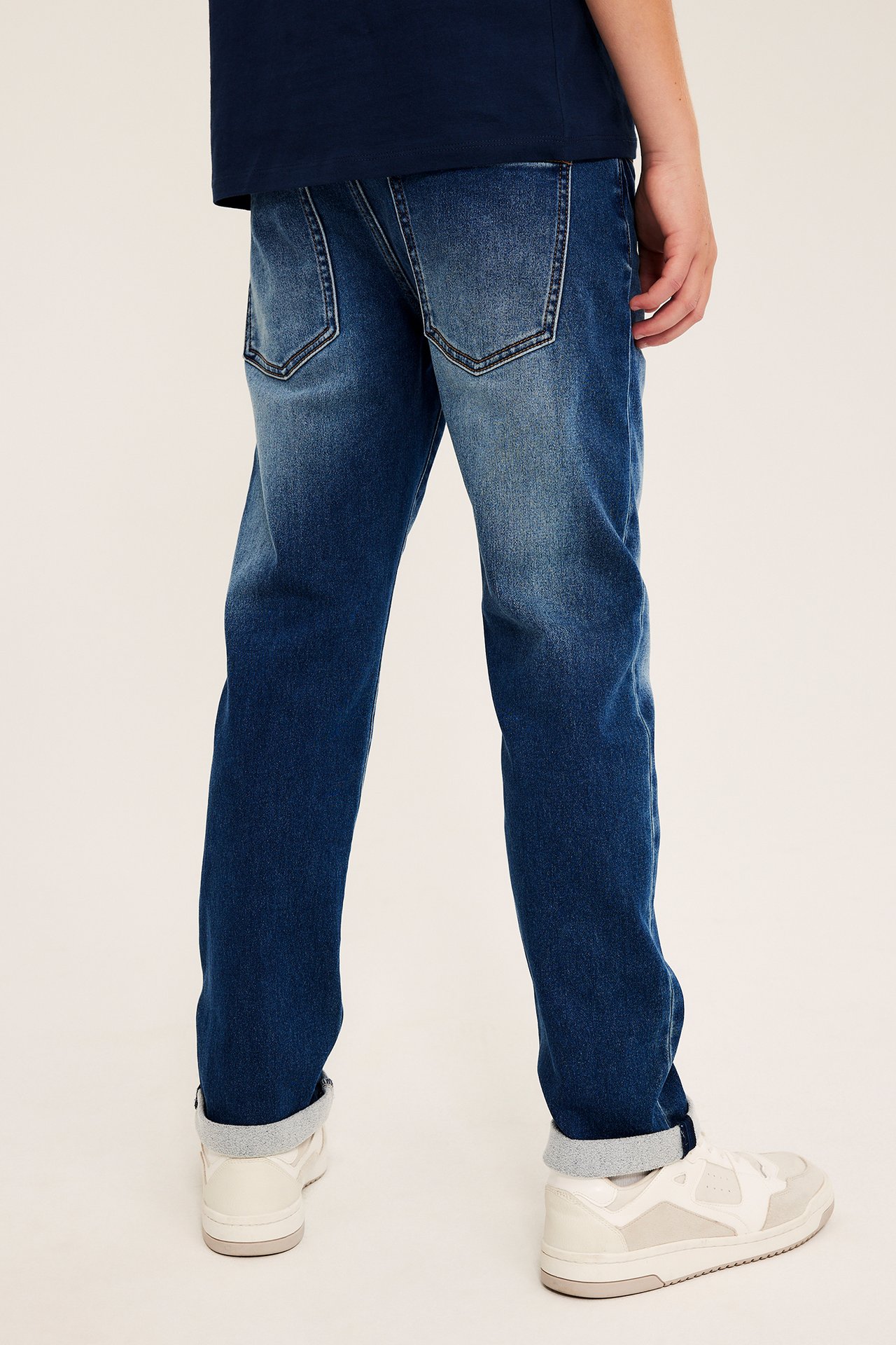 Bakifrån av blå jeans med synliga bakfickor, stylade med mörk topp och ljusa sneakers.