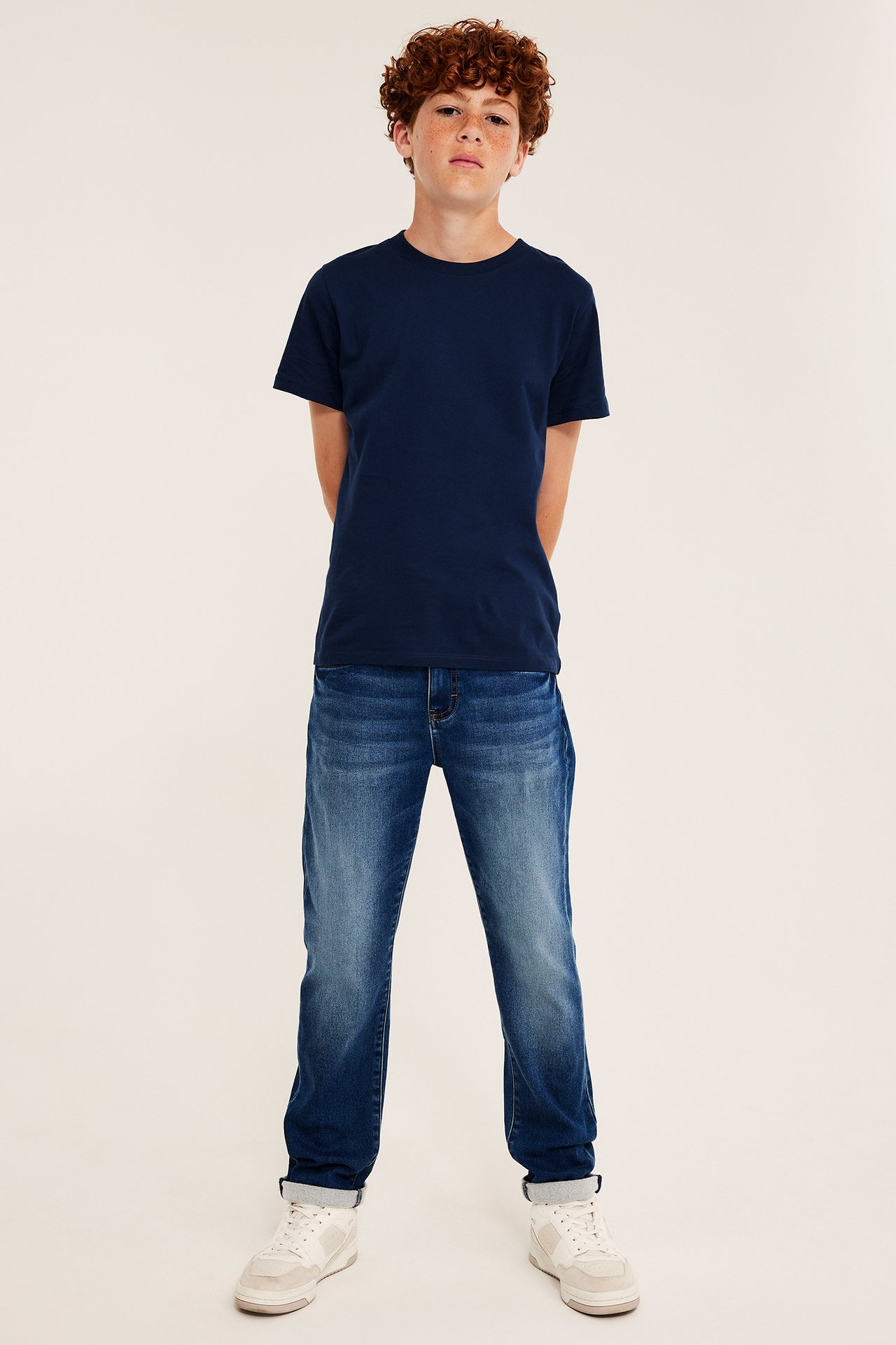 Framsida av barn i marinblå kortärmad t-shirt, blå jeans och vita sneakers.